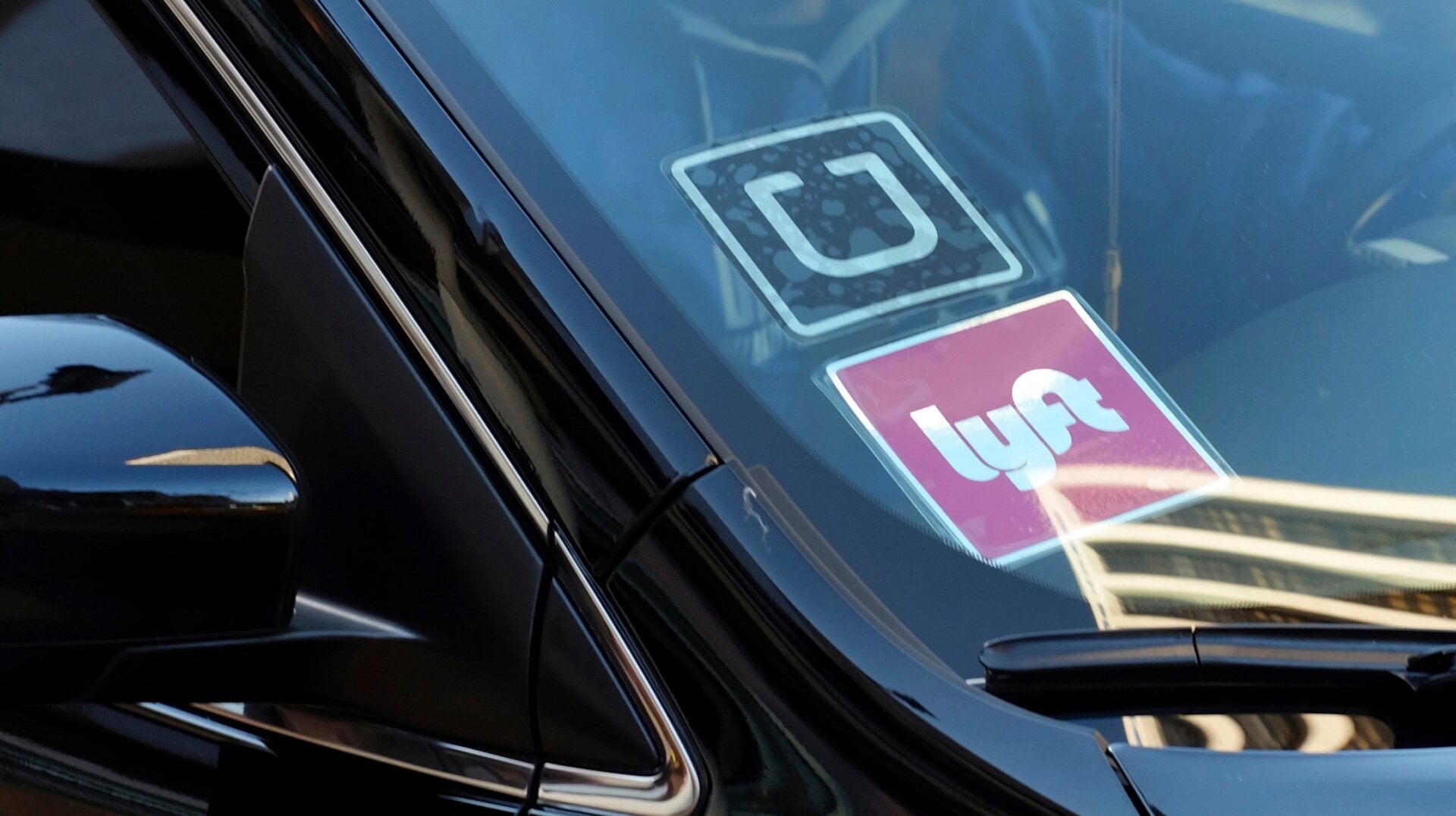 A ride share car displays Lyft and Uber stickers on its front windshield in downtown Los Angeles.