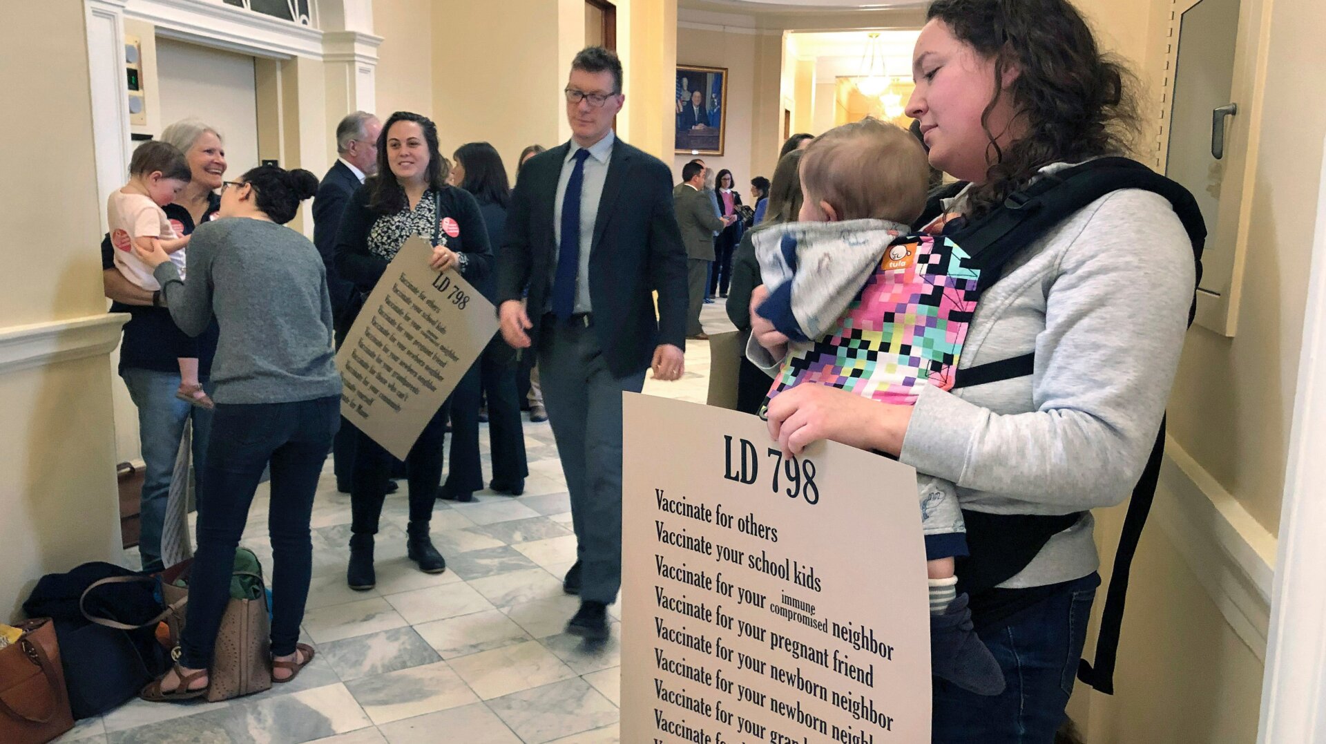 A woman holds her daughter with other mothers in a hallway, Thursday, May 2, 2019, at the Statehouse in Augusta, Maine, where the Senate was considering a bill ending non-medical vaccine exemptions. The bill passed and was signed by Governor Janet Mills (D) on Friday.