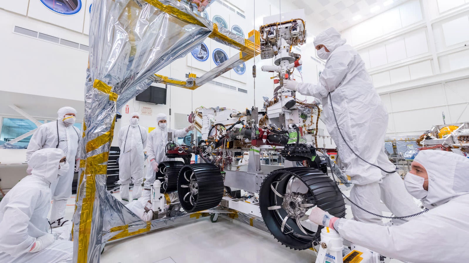 Jet Propulsion Lab engineers install three right-side wheels on the Mars 2020 rover.