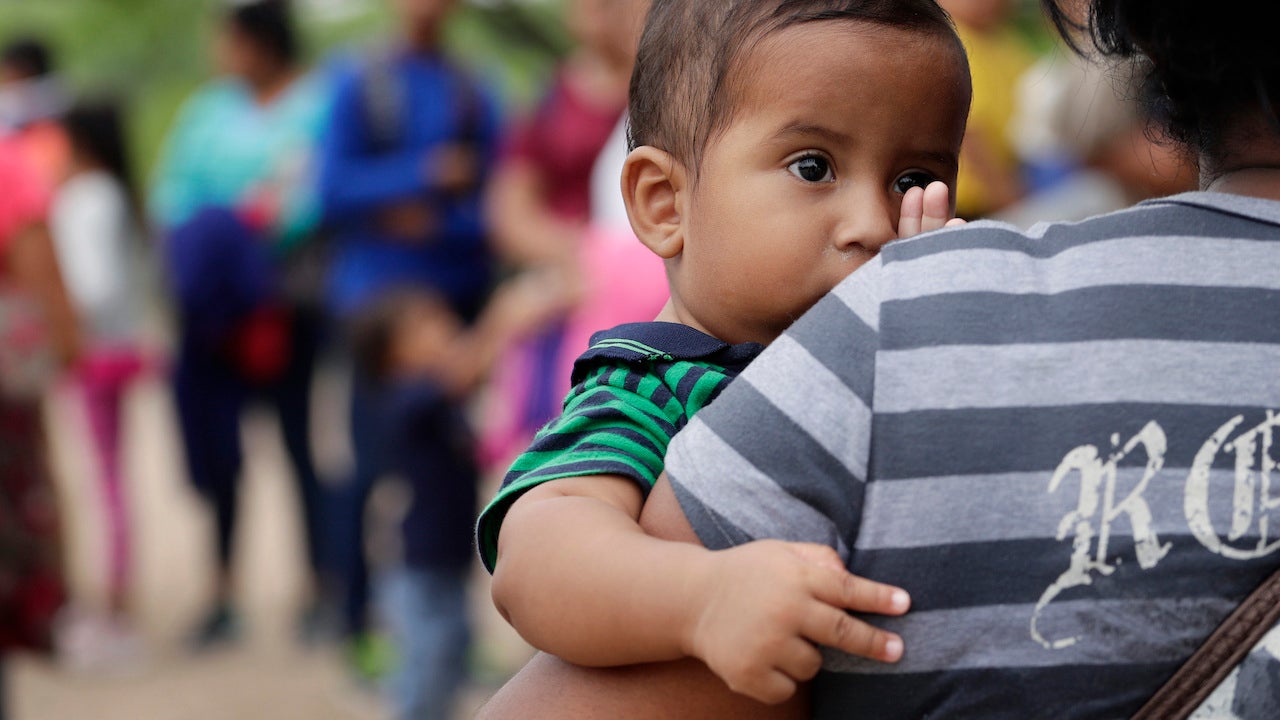 In this March 14, 2019 photo, a 7-month old boy peers over the shoulder of his mother as they wait for DHS agents to apprehend them at the U.S.-Mexico border near McAllen, Texas.