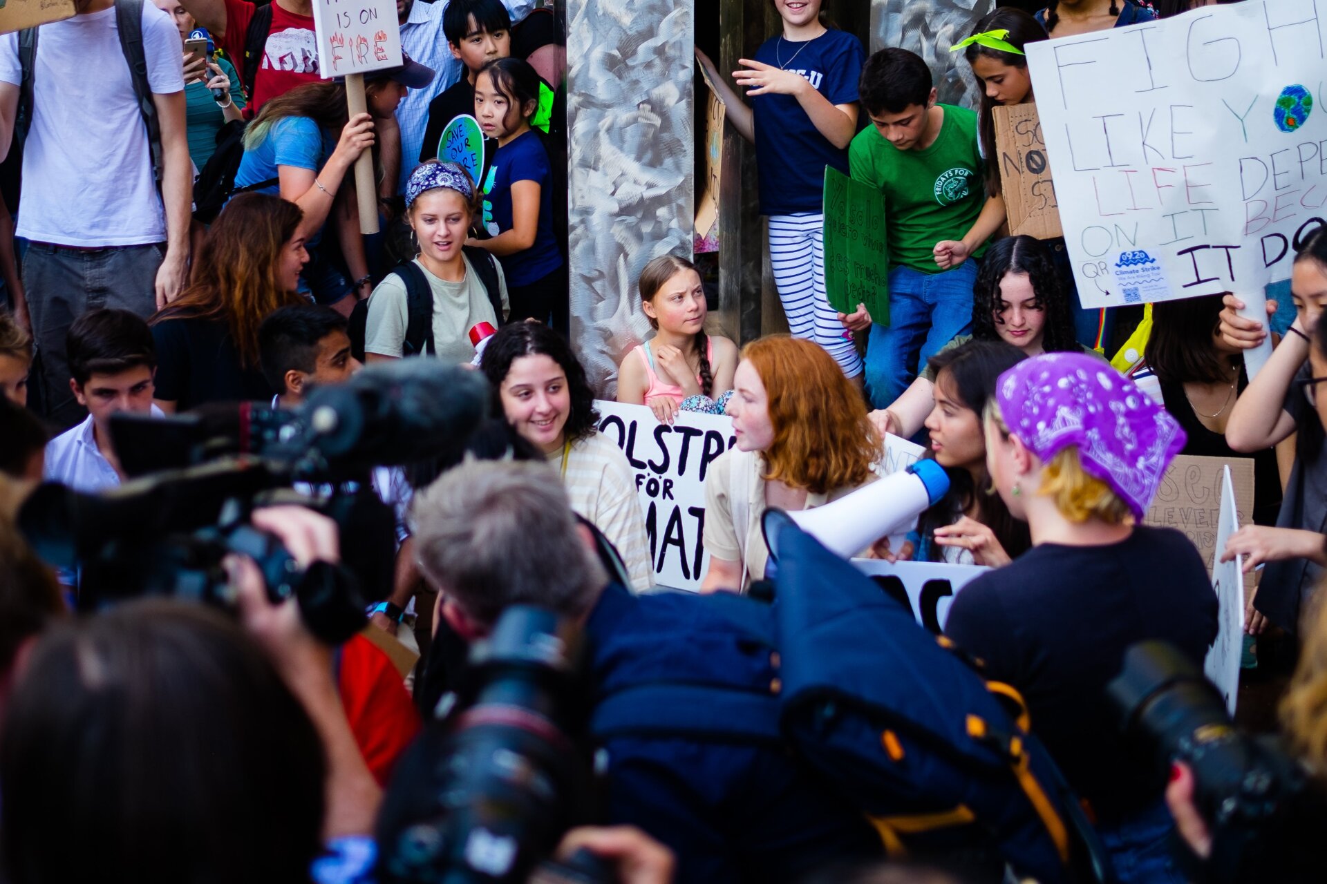 Greta Thunberg sits in the middle of American activists and the press.