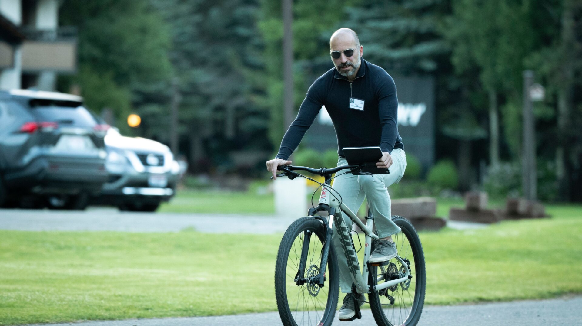 Dara Khosrowshahi using some sort of tablet while riding a bike, a photo I will never get sick of looking at
