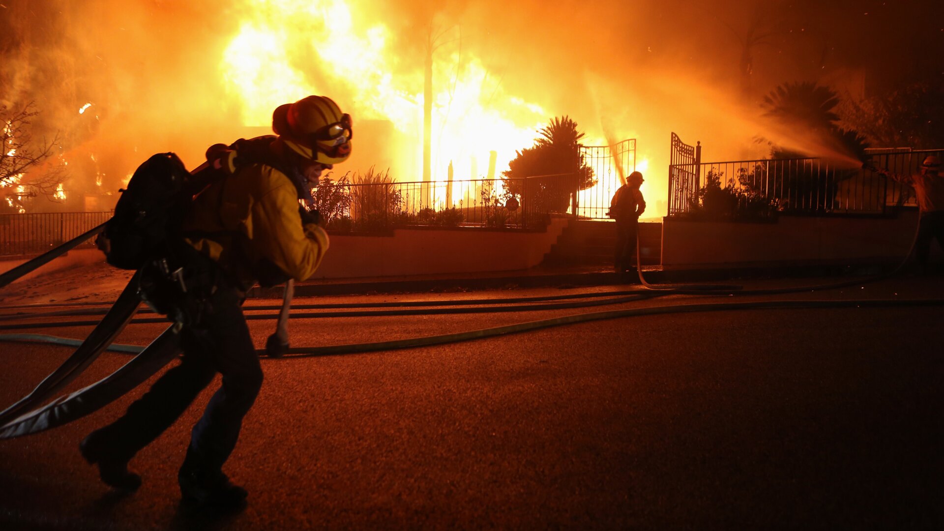 Firefighters work on a house fire during the Saddleridge Fire in the early morning hours on October 11, 2019 in Porter Ranch, California.
