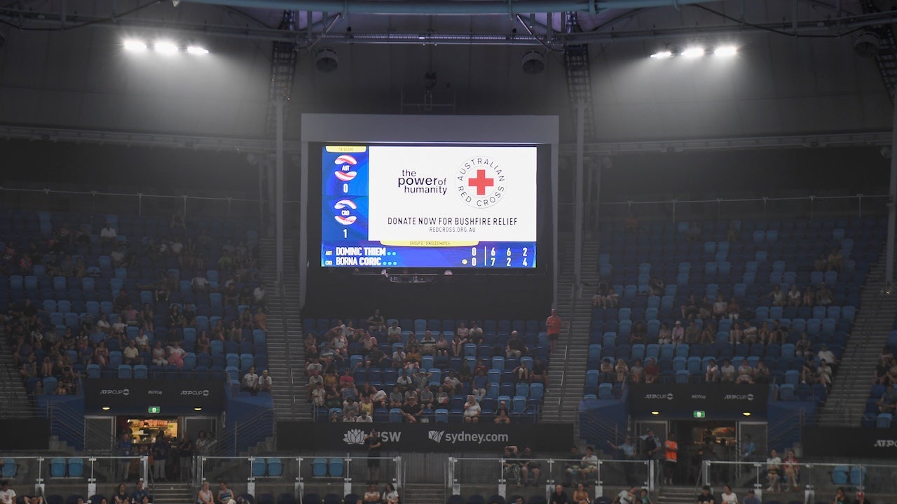 A message asking for donations for the Red Cross is displayed on a screen while fans sit in the haze created by the Australian bushfires at a tennis match in Sydney on January 4, 2020