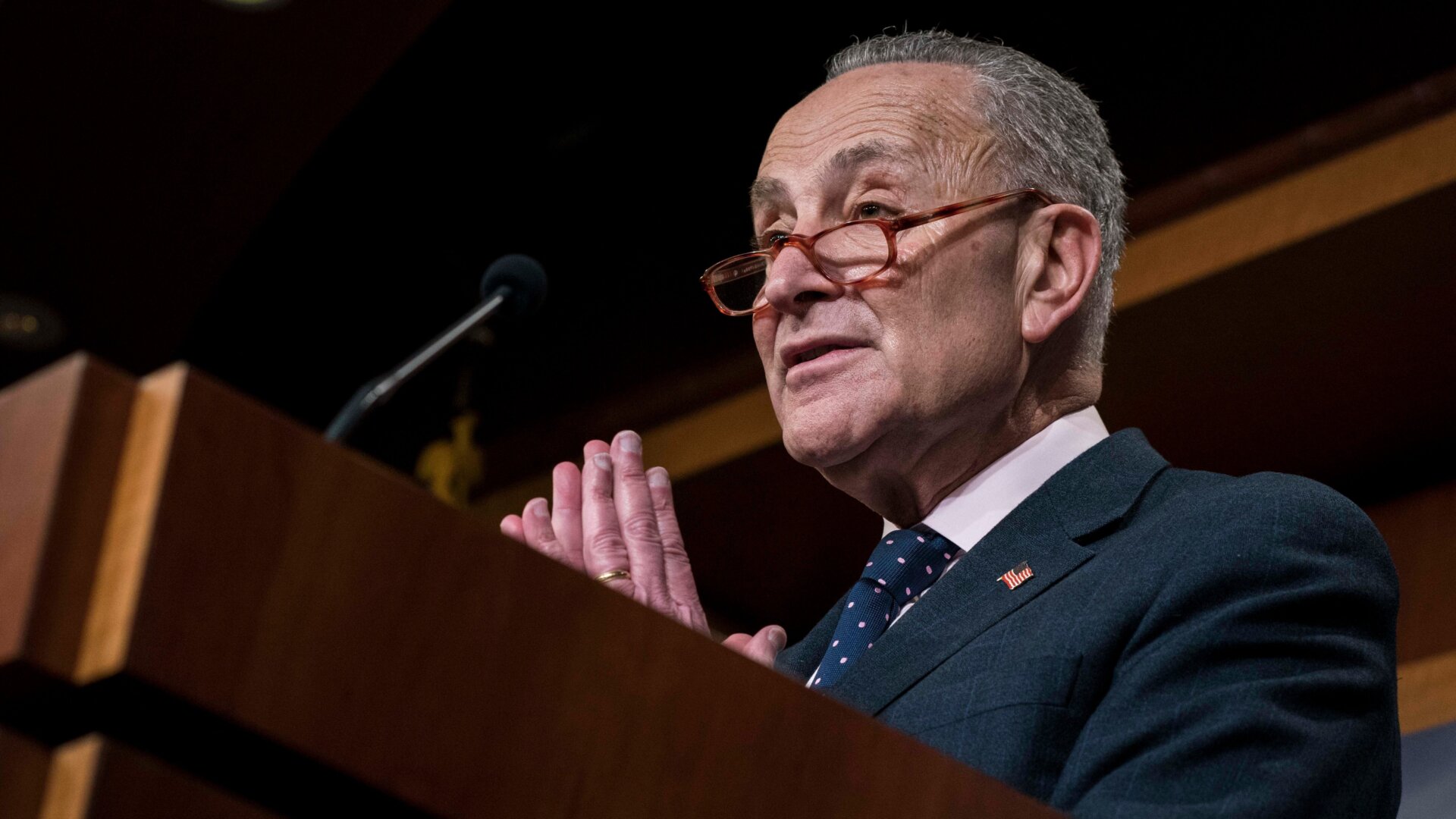 Chuck Schumer in glasses, speaking at a podium