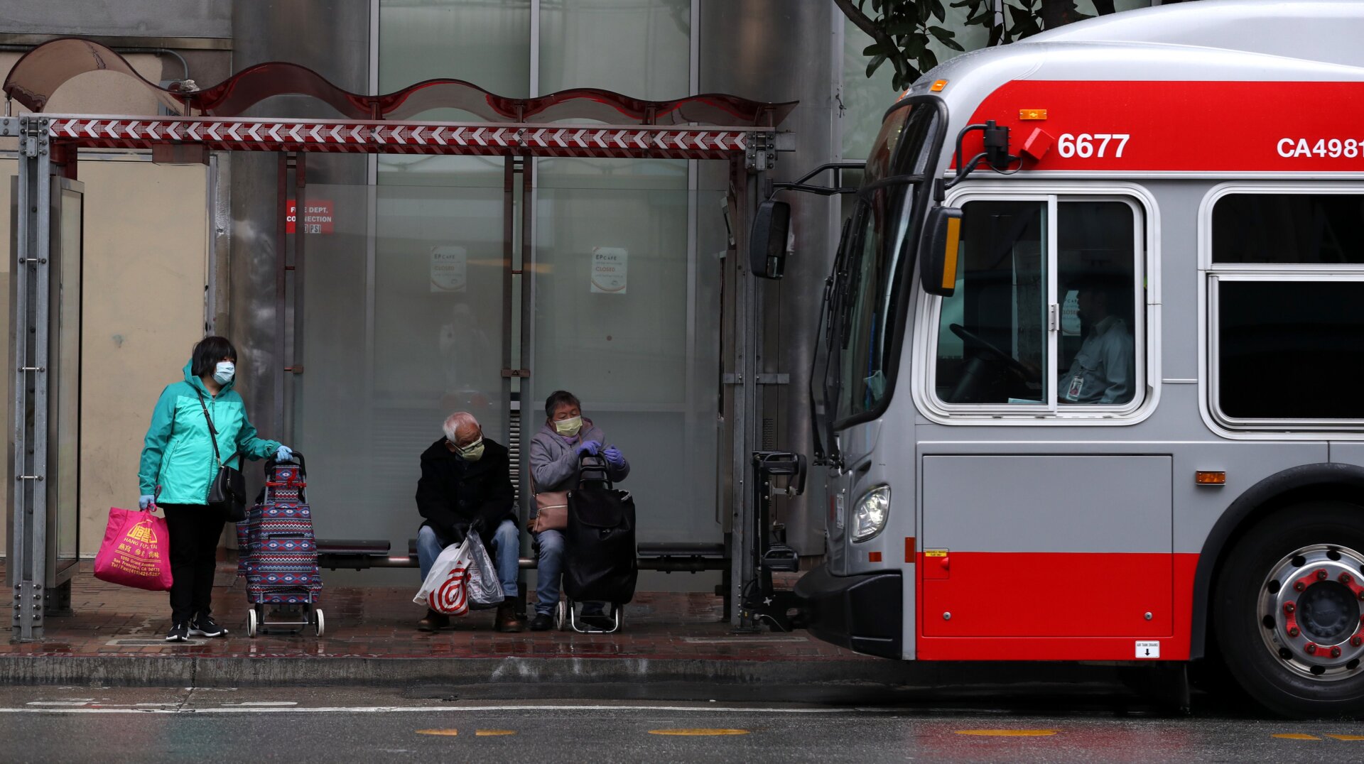 People wear masks as they wait in a bus shelter for a San Francisco MUNI bus amid the coronavirus pandemic.
