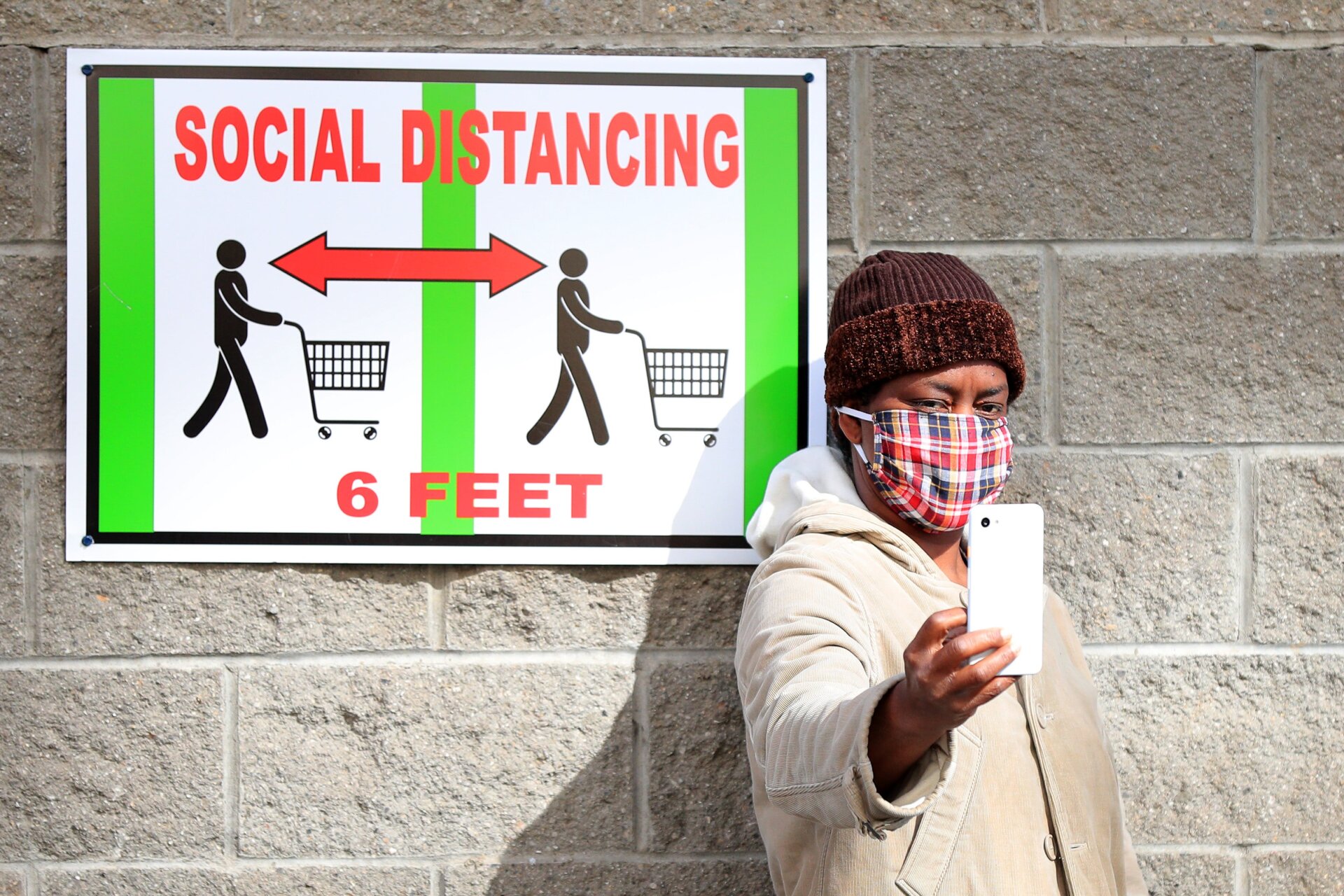 A customer takes a selfie in front of a sign recommending social distancing while waiting to enter the Industry City Costco store on April 28, 2020 in the Brooklyn borough of New York City.