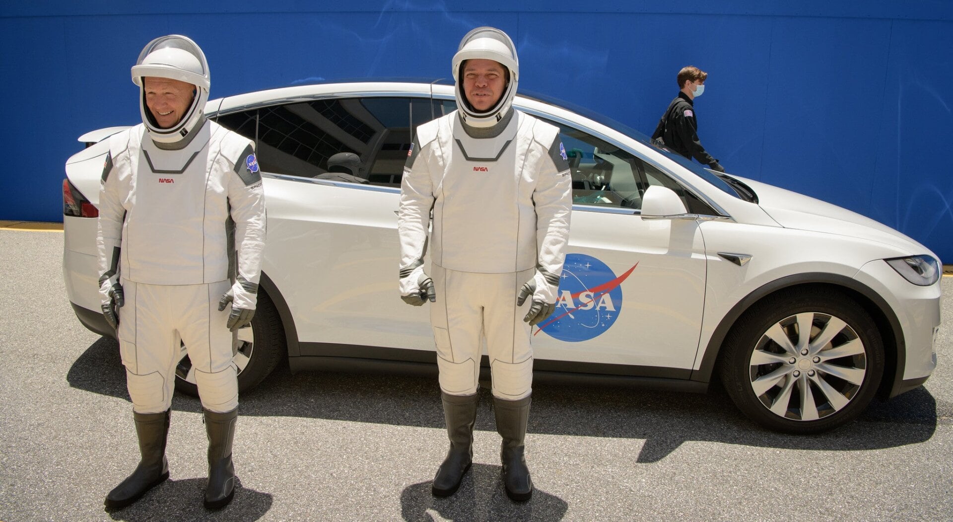 NASA astronauts Douglas Hurley and Robert Behnken wearing SpaceX spacesuits and with a Tesla Model X behind them.