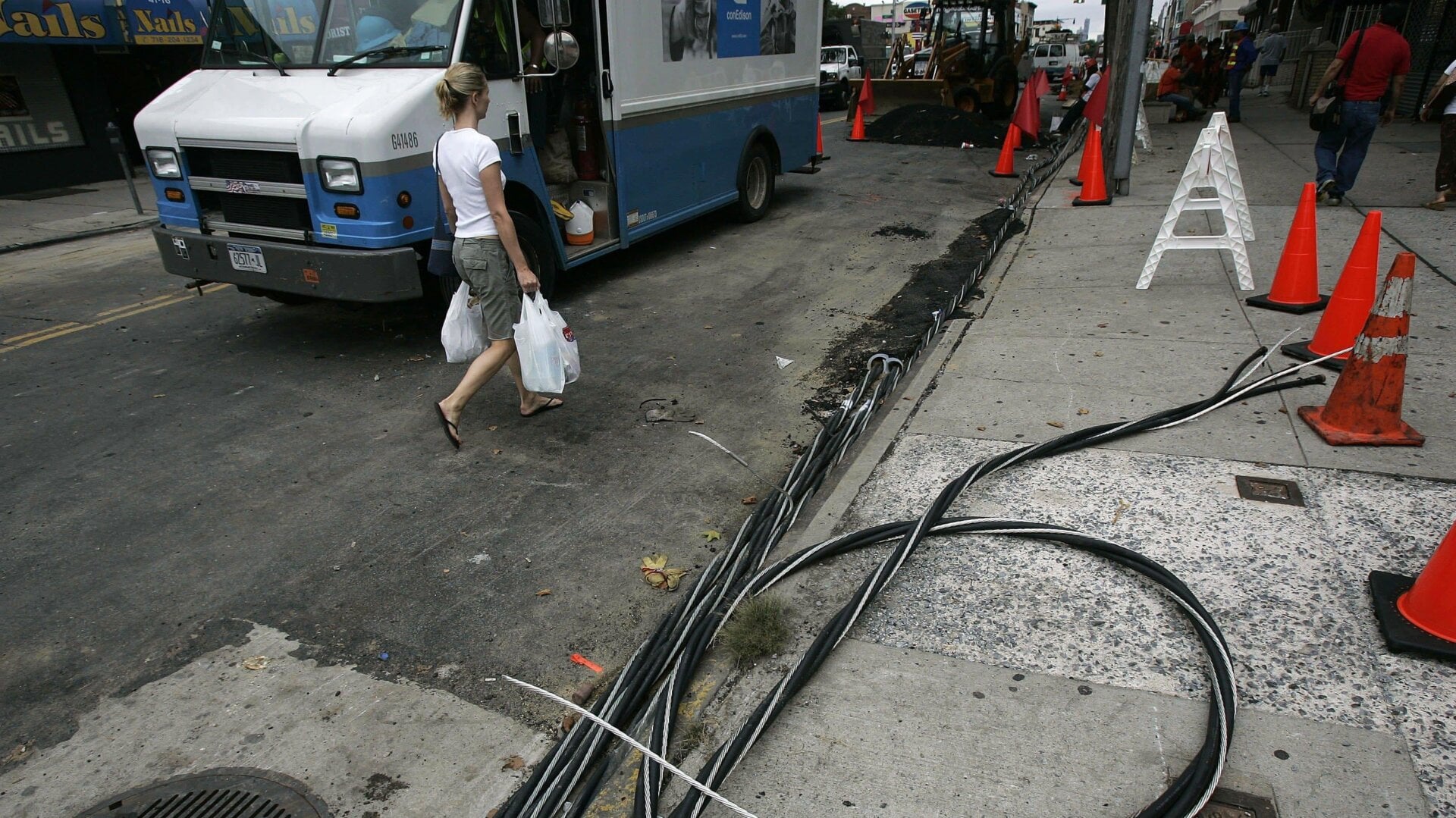 A woman walks past power lines on the sidewalk as workers try to restore electrical service July 23, 2006 in the Queens borough of New York City.