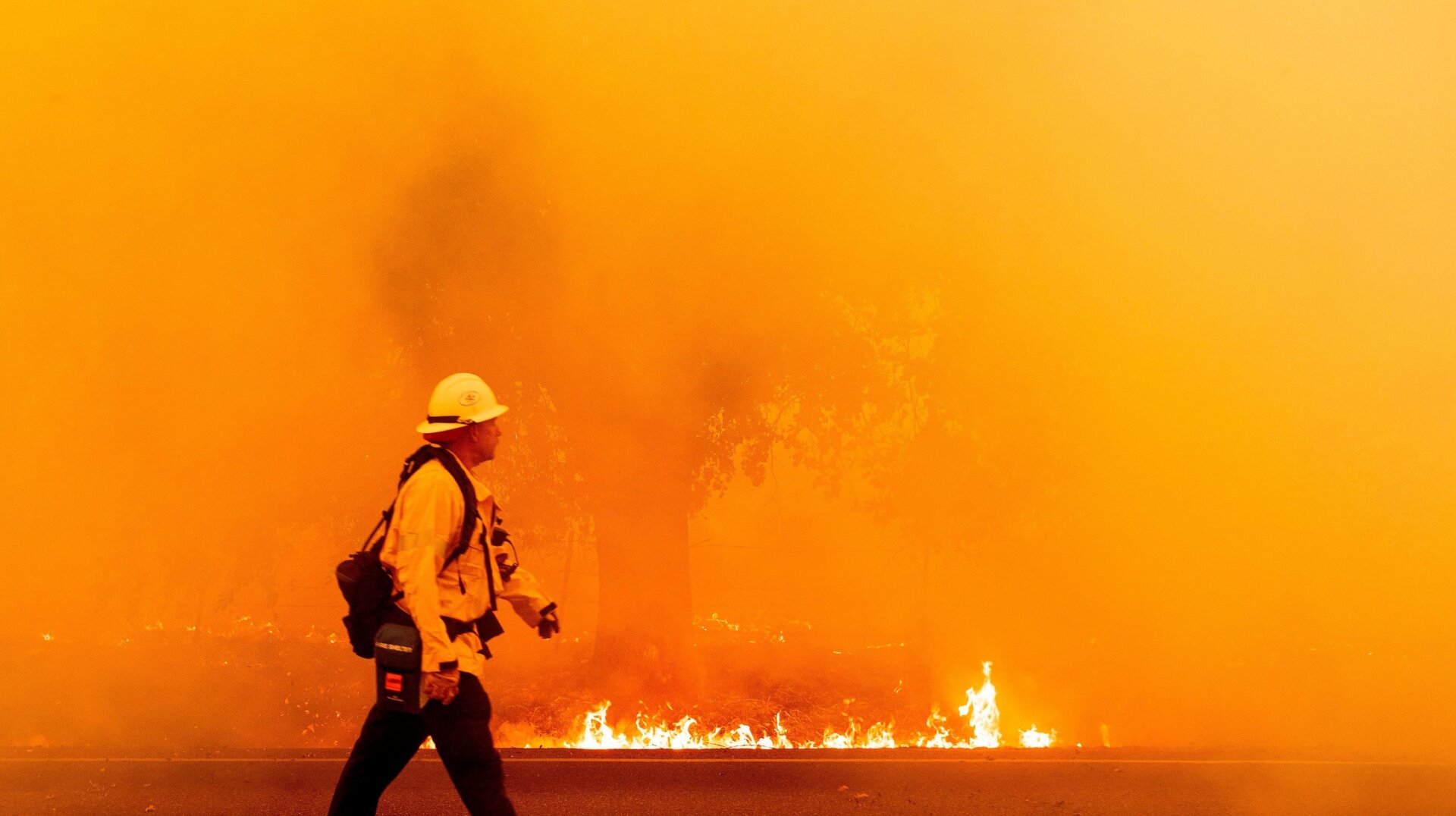 A firefighter walks in front of a blaze.