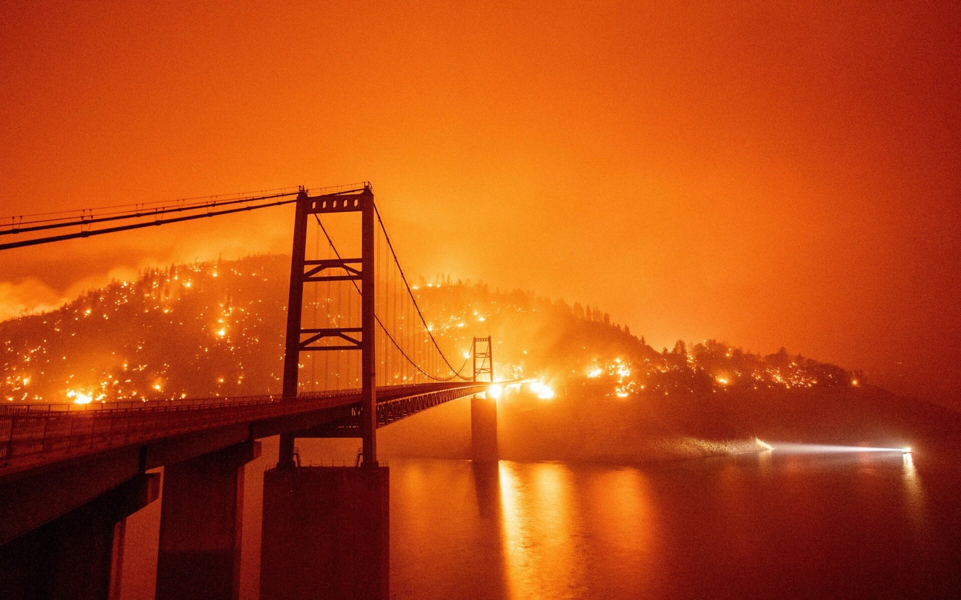 A boat motors by as the Bidwell Bar Bridge is surrounded by fire in Lake Oroville during the Bear fire in Oroville, California on September 9, 2020.