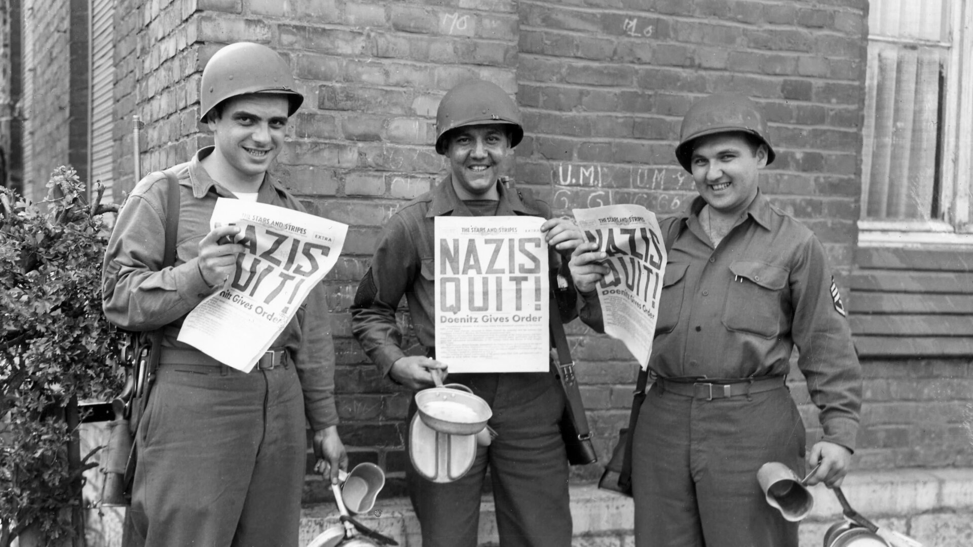 U.S. Ninth Army soldiers smiling while holding copies of ‘The Stars and Stripes’ announcing Germany’s surrender in World War II. 8th May 1945.
