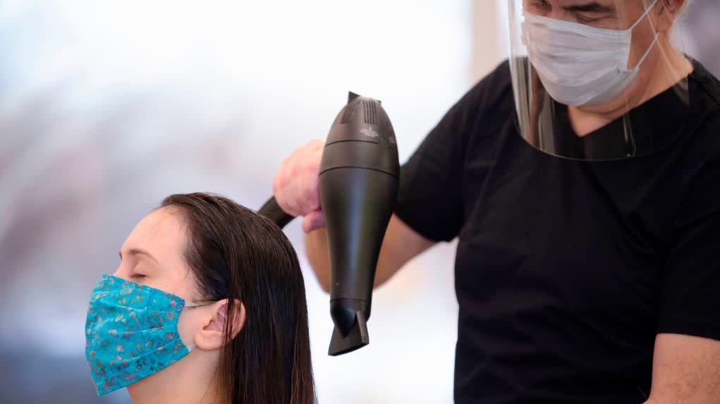 Stylist Neck Gunes (R) blow-dries his customer Jennifer Nardelli’s hair while wearing a face mask and shield at Saint Germain Hair Salon in Washington, D.C., on May 29, 2020,