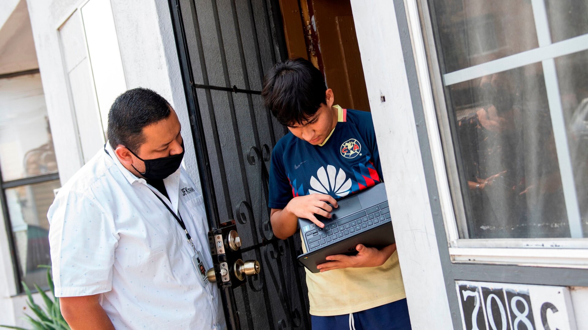 David Palencia from JFK helps Angel, 13, to connect his computer to the Wifi Hotspot provided by a parked van from JFK Transportation in order to follow his online classes, September 16, 2020, in Santa Ana, California.