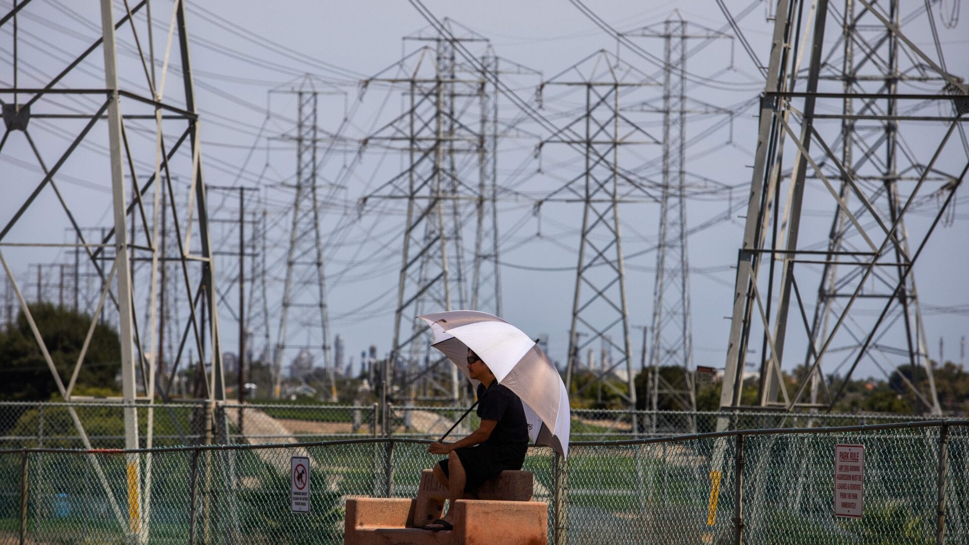 A man sits in the shade of his umbrella at the Dog Park under high tension power lines in Redondo Beach, California on Aug. 16, 2020. California ordered rolling power outages for the first time since 2001 as a statewide heat wave strained its electrical system.