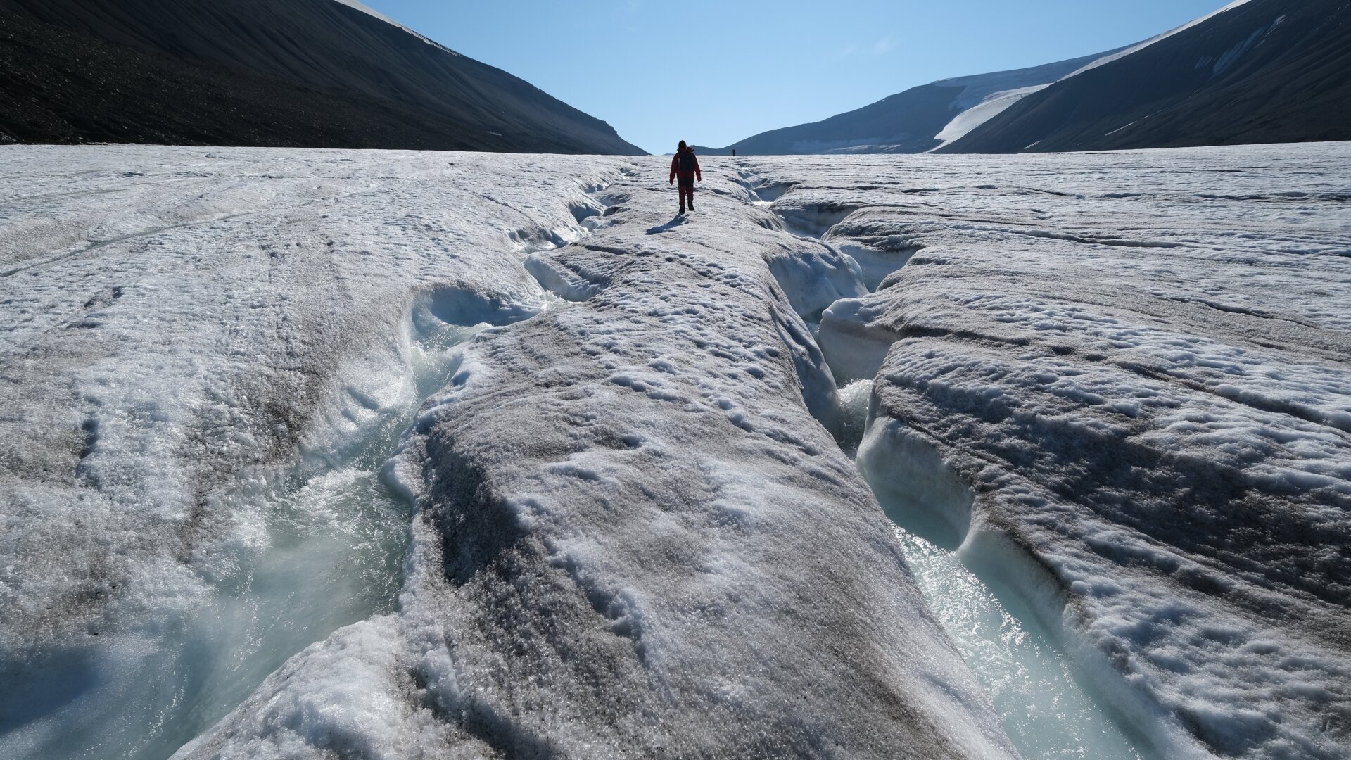 A hiker walks among winding channels carved by water on the surface of the melting Longyearbreen glacier during a summer heat wave on Svalbard archipelago on July 31, 2020.
