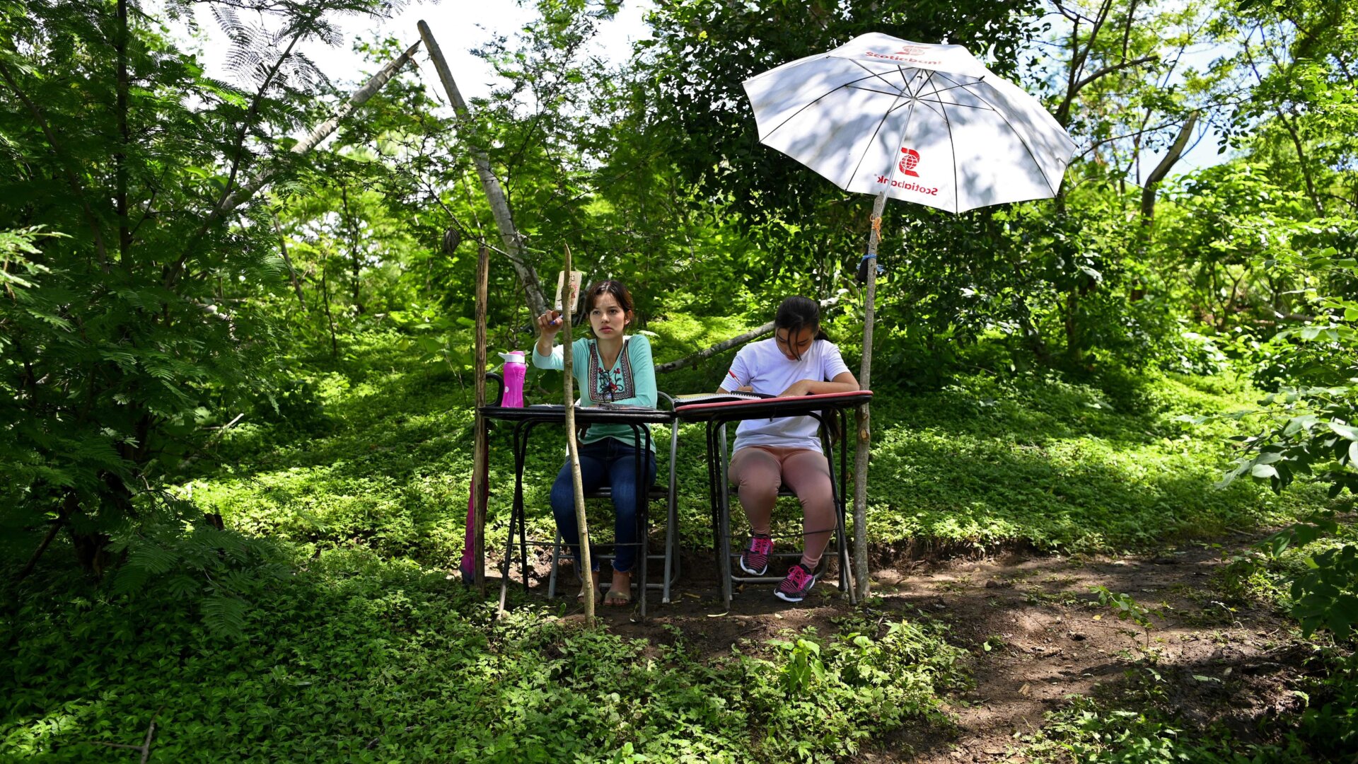 Sisters and university students, Matilde (L) and Marlene Pimentel, do their schoolwork from a hilltop where they can reach internet signal in El Tigre, El Salvador, on August 21, 2020.