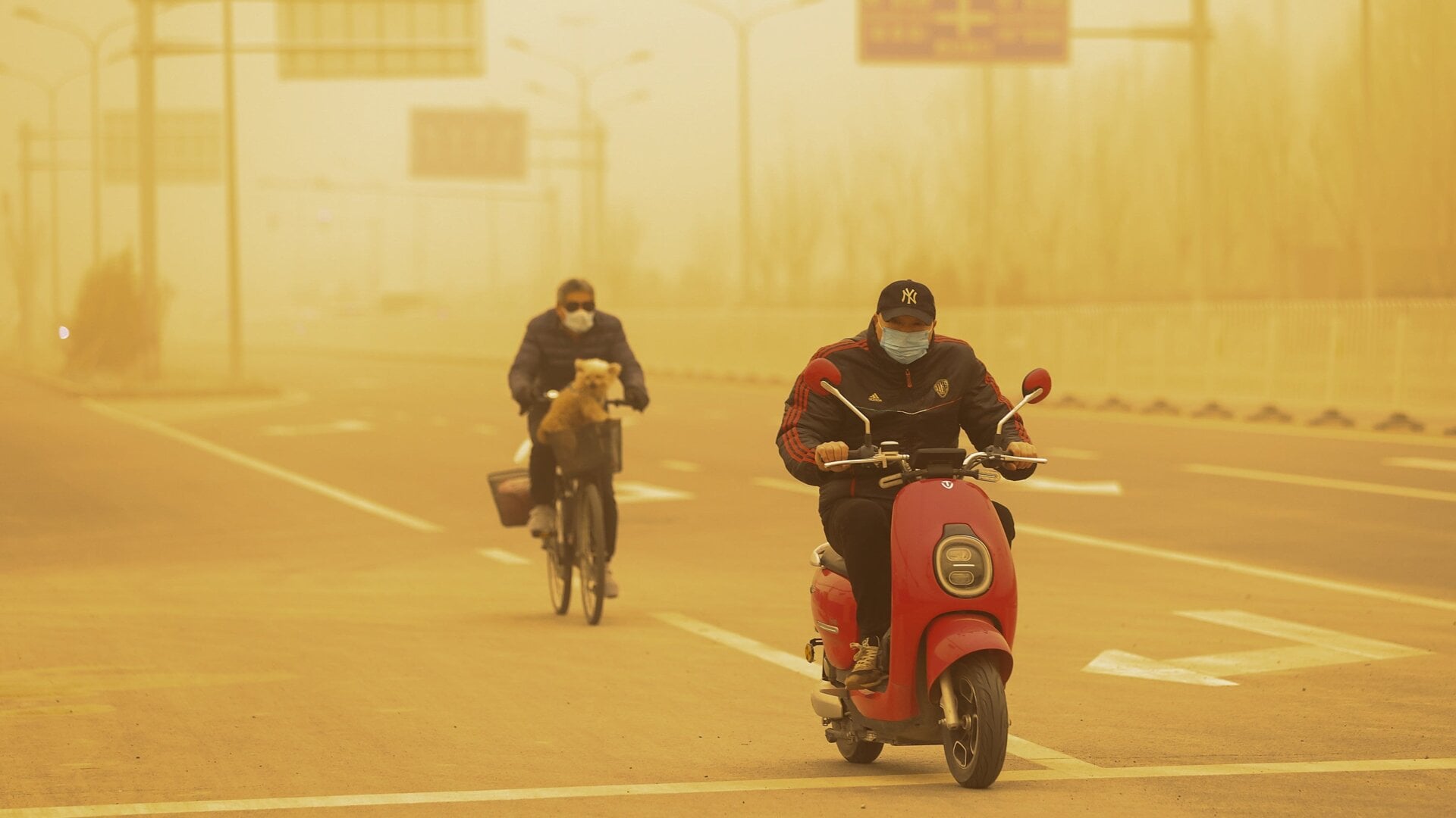 People wearing protective masks ride their bikes along a street during a sandstorm on March 15, 2021 in Beijing, China. The Chinese capital and the northern parts of the country was hit with a sandstorm on Monday, sending air quality indexes of PM 2.5 and PM 10 ratings into the thousands and cancelling flights.