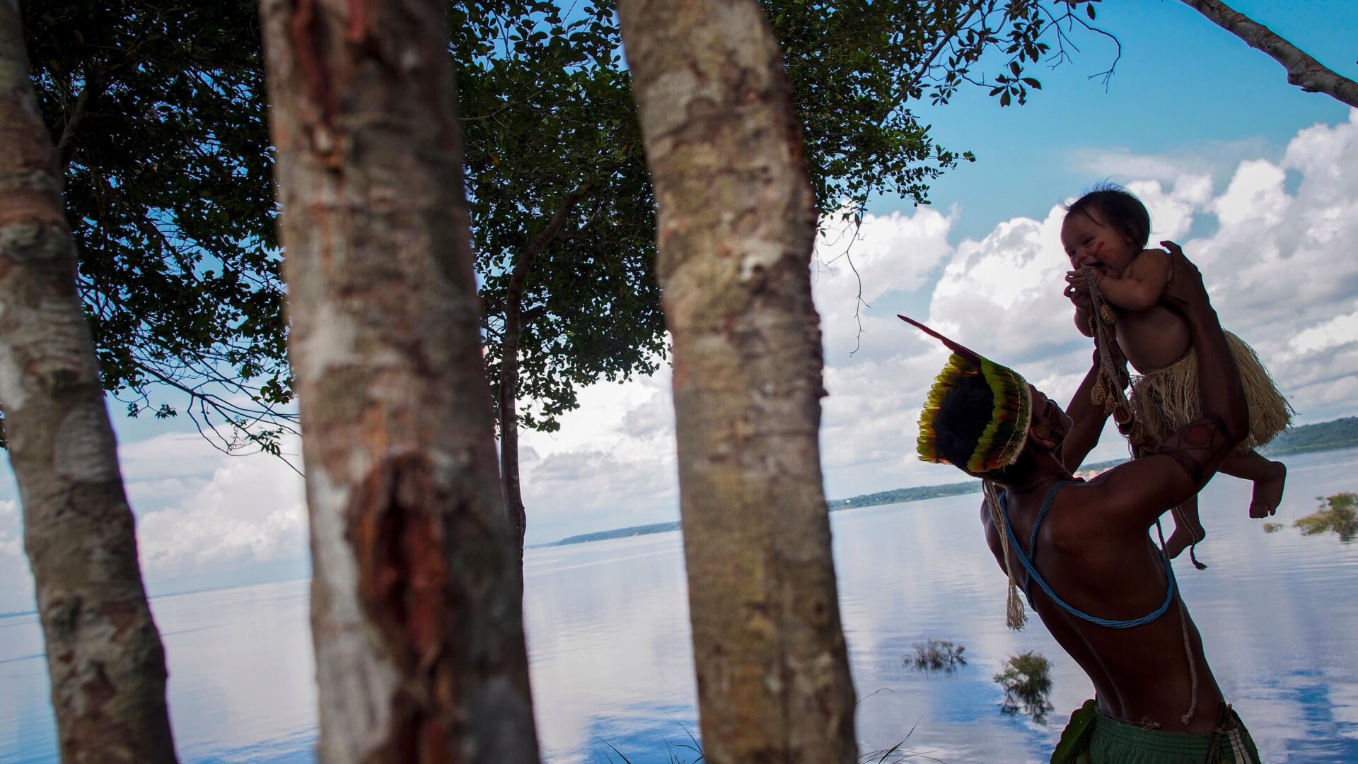 A Dessana indigenous man plays with a baby by the Negro River at the Tupe Reservation in the outskirts of Manaus, Amazonas, Brazil.