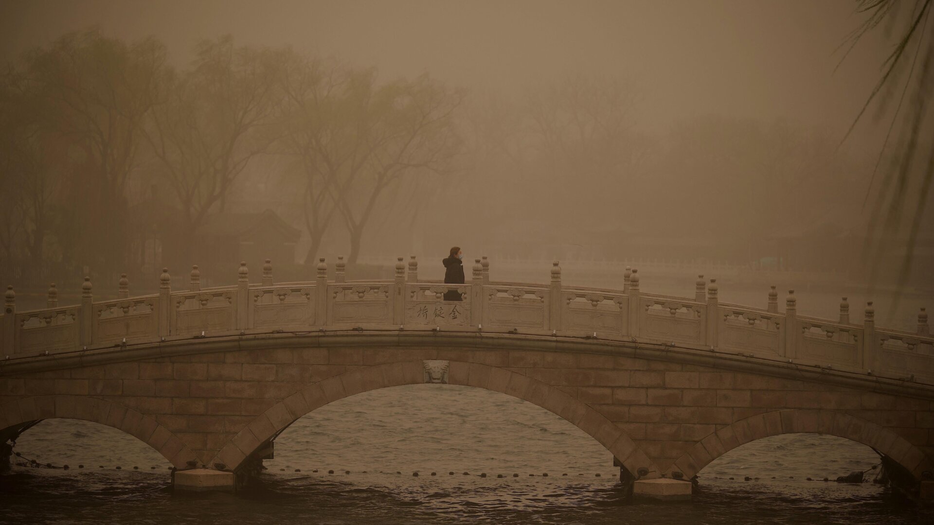 A woman crosses a bridge at Houhai lake during a sandstorm in Beijing on March 15, 2021.  