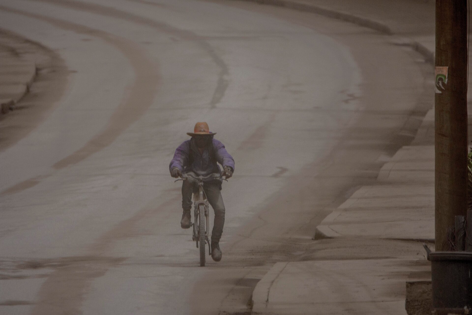 A man rides his bicycle along the main Black Rock road, covered with ash coming from the eruption of La Soufrière volcano in the neighboring island of St. Vincent, on the outskirts of Bridgetown, Barbados, on Sunday, April 11.