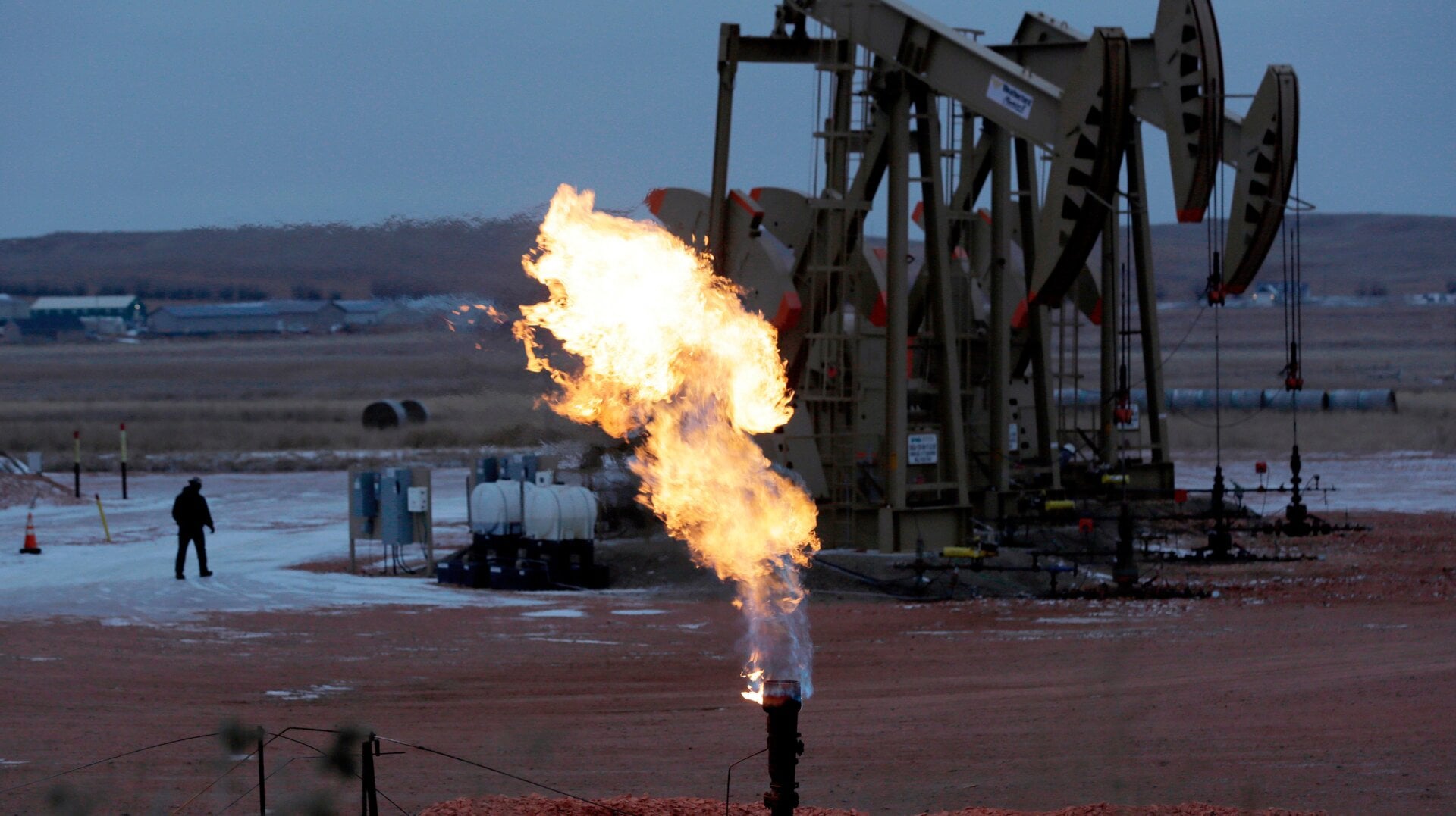 A natural gas flare in front of pump jacks.