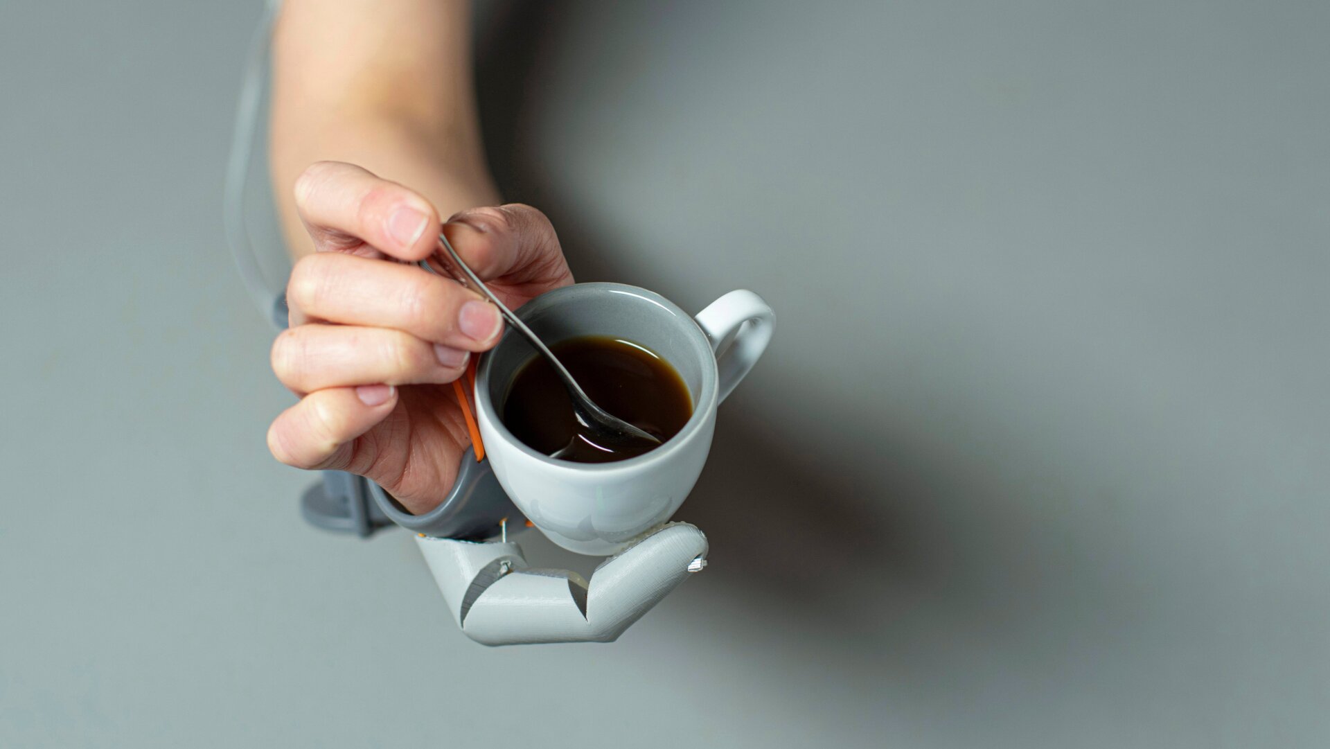 A person supporting a coffee cup with the Third Thumb, while stirring a spoon with their natural fingers.
