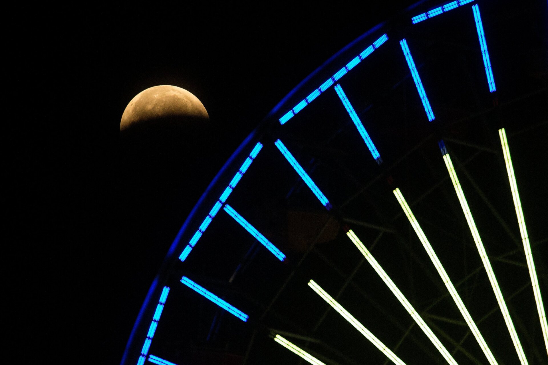 The lunar eclipse progresses is seen behind a ferris wheel over Santa  Monica Beach in Santa Monica, Calif., Wednesday, May 26, 2021.