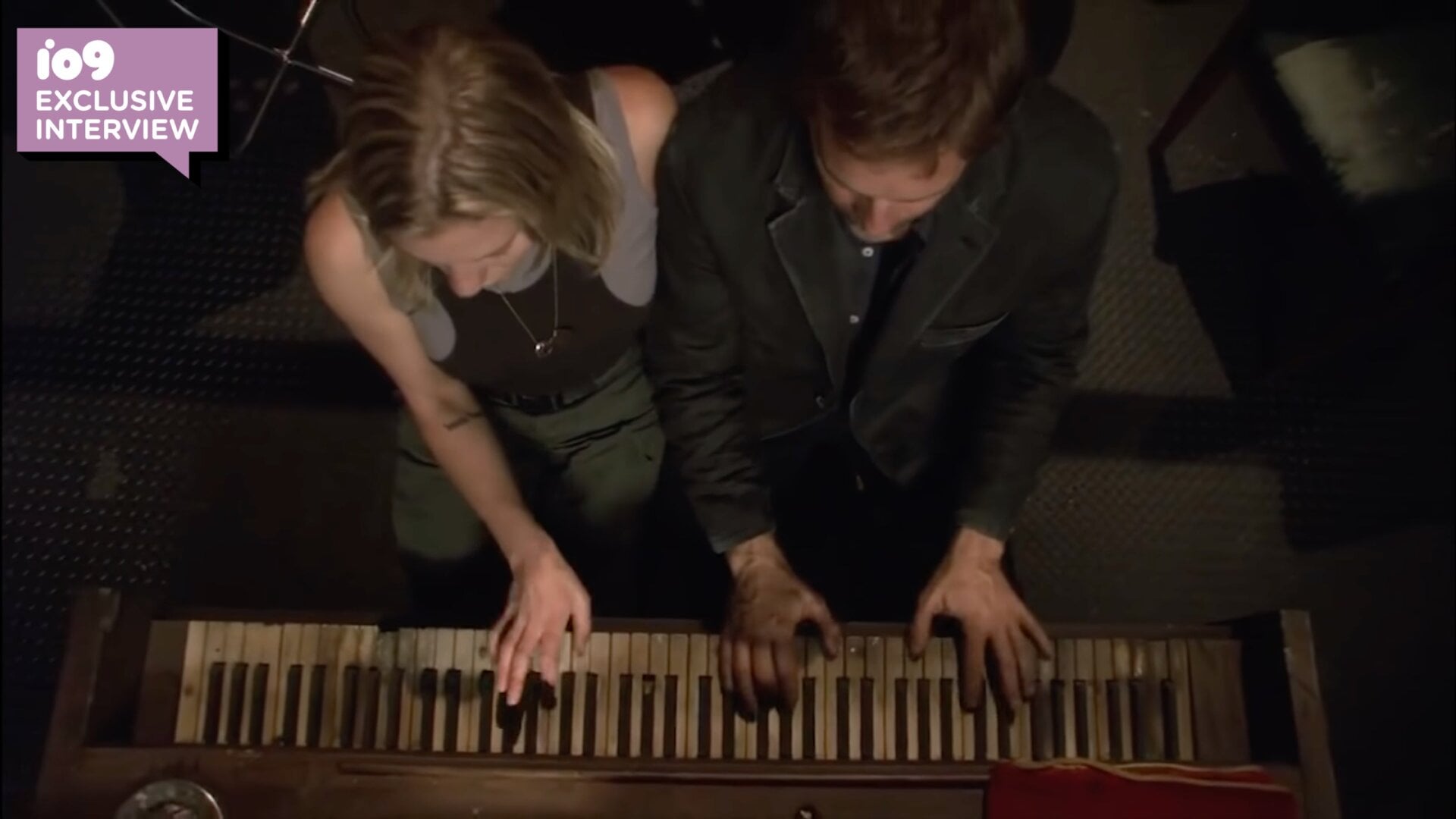 An enigmatic stranger (Roark Critchlow) gives Starbuck (Katee Sackhoff) a piano lesson.