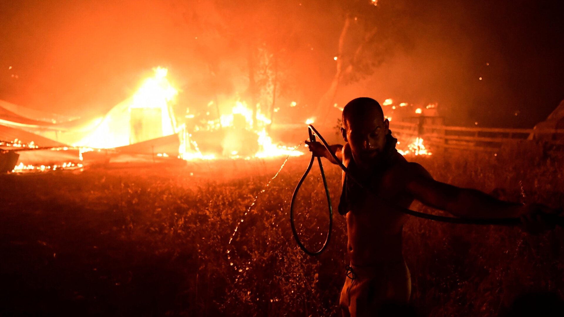 A man uses a water hose during a wildfire in Adames area.
