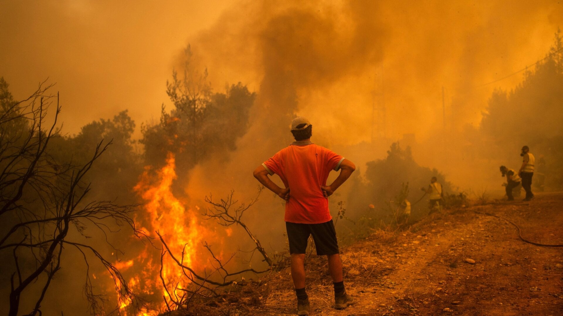 A volunteer watches as firefighters use a water hose to extinguish the blaze of a forest fire in the village of Glatsona on Evia (Euboea) island, on August 9, 2021.