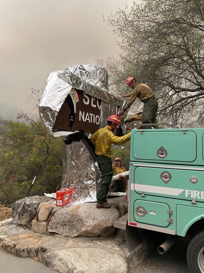 Firefighters wrap a historic Sequoia National Park sign in protective foil.