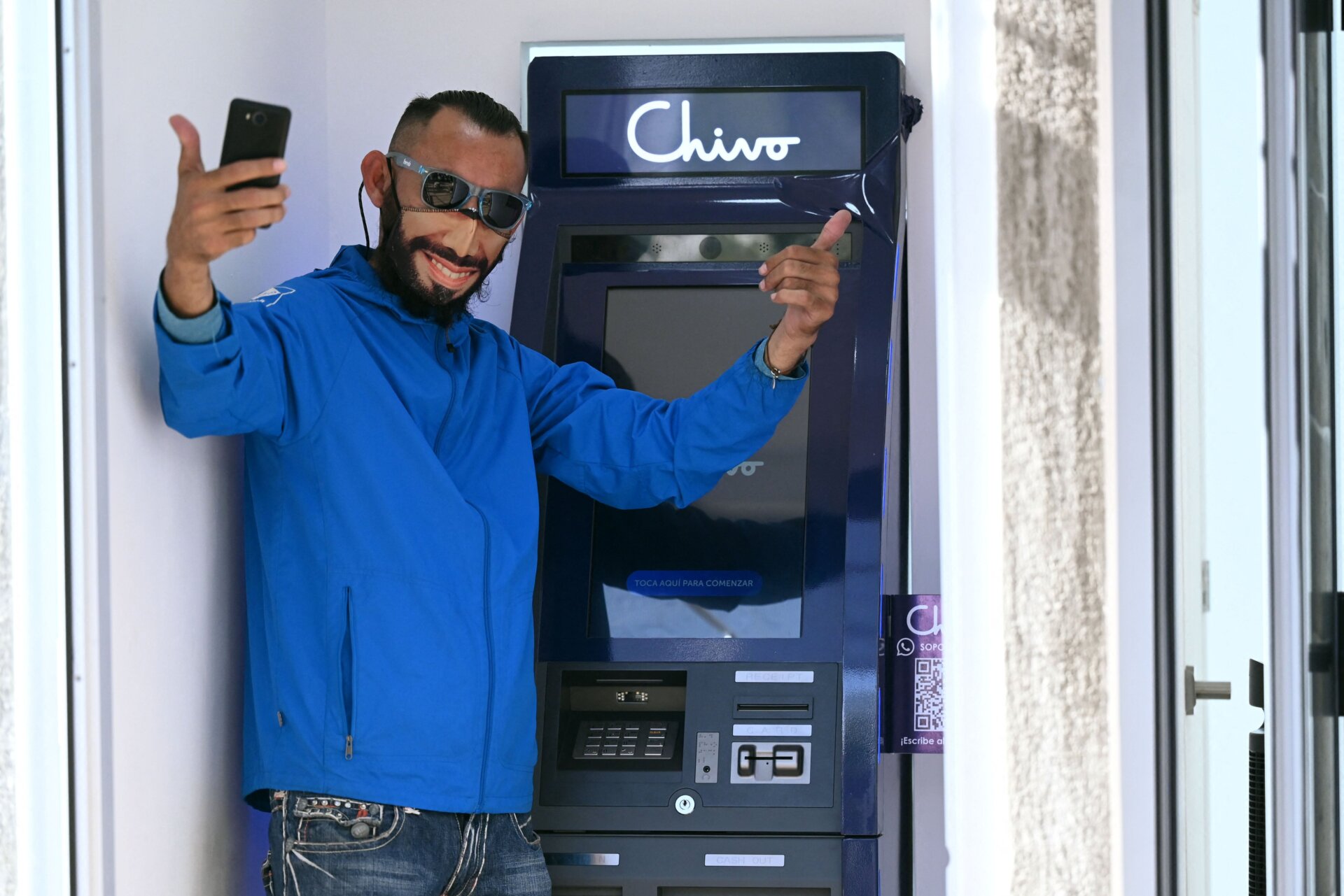 A man wearing a protective face mask with the image of Salvadoran  President Nayib Bukele pose for a picture at a bitcoin ATM in San  Salvador, on September 7, 2021.