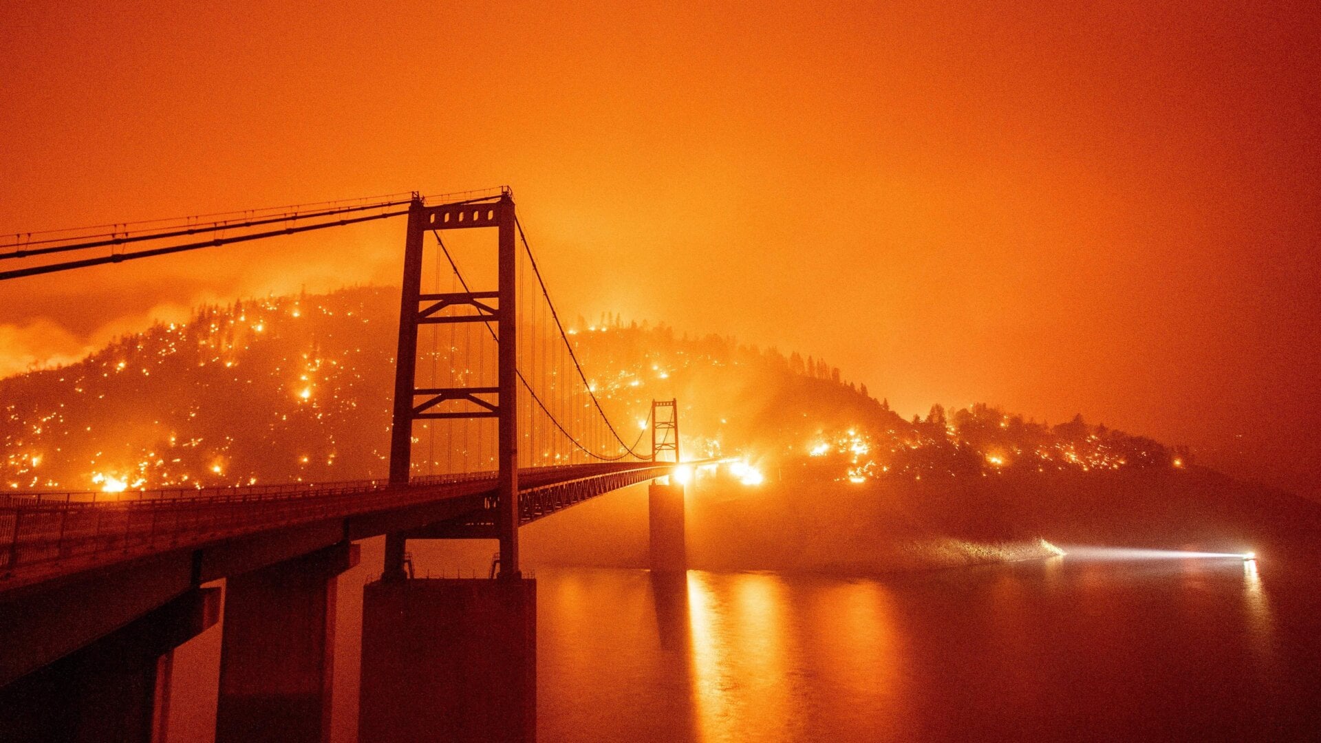 A boat motors by as the Bidwell Bar Bridge is surrounded by fire in Lake Oroville during the Bear fire in Oroville, California on Sept. 9, 2020.
