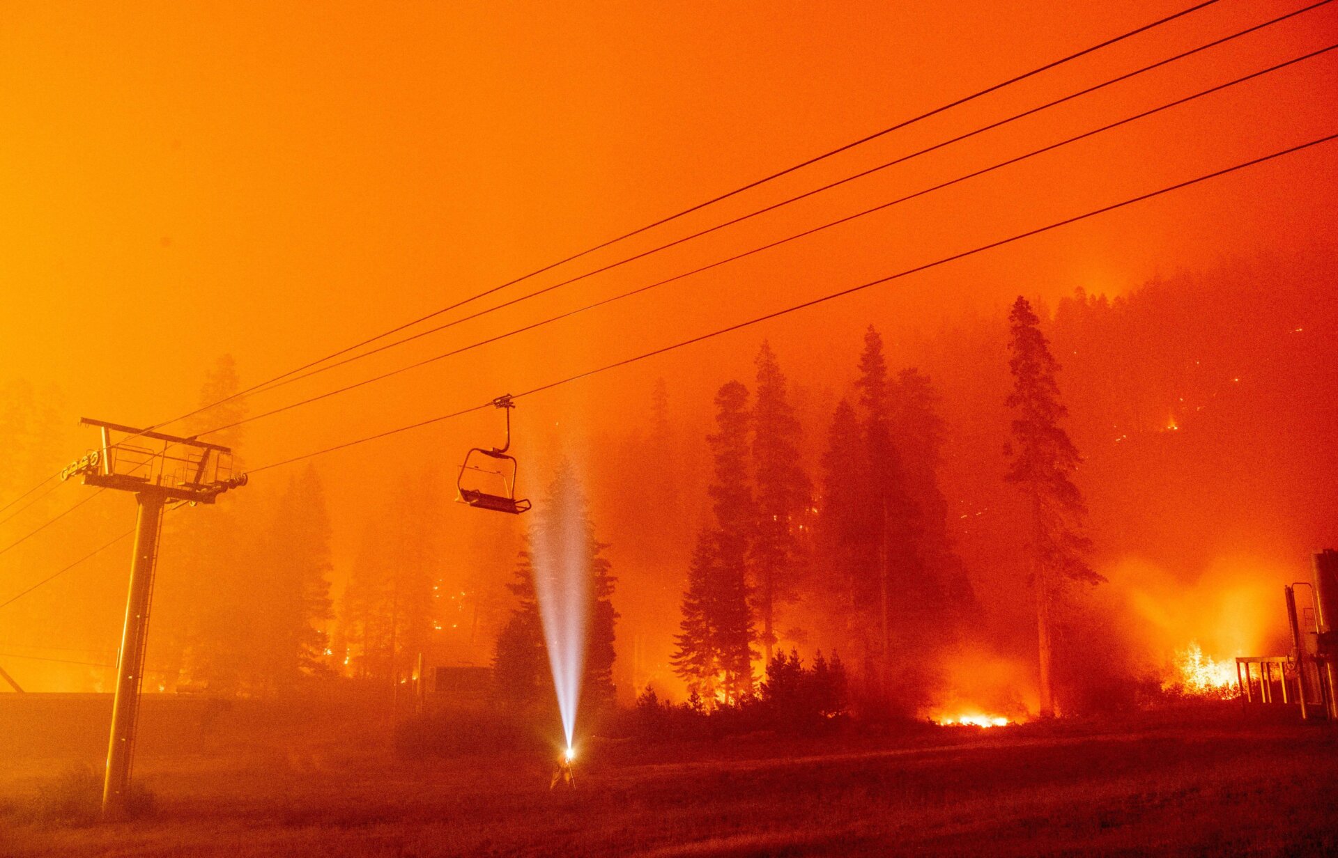 A photographer shines a flashlight towards a chair lift as flames surround Sierra-at-Tahoe Resort, a skiing area, during the Caldor fire in Twin Bridges, California, on Aug. 30, 2021