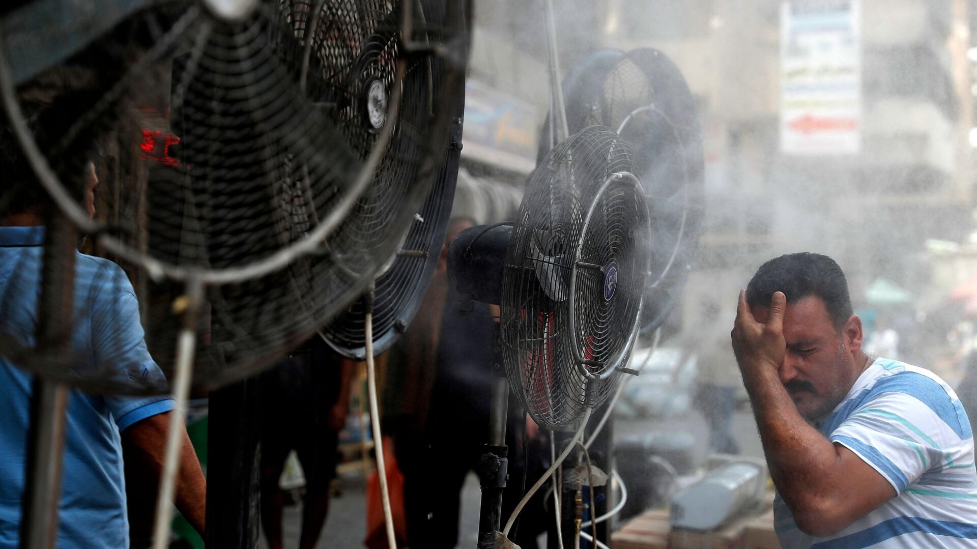 A man stands by fans spraying air mixed with water vapor deployed by donors to cool down pedestrians along a street in Iraq’s capital Baghdad on June 30, 2021 amidst a severe heat wave.