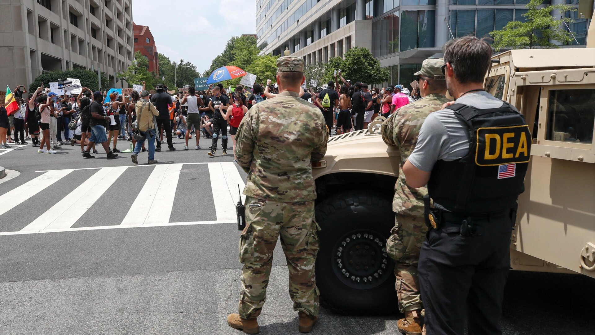 As a Drug Enforcement Agency police office and National Guard soldiers watch, demonstrators protest Saturday, June 6, 2020, in Washington, over the death of George Floyd.