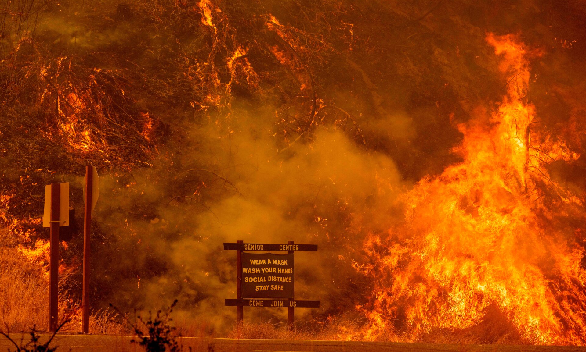 A sign warning people about Covid-19 is surrounded by flames during the Hennessey Fire near Lake Berryessa in Napa, California,, on Aug. 18, 2020.