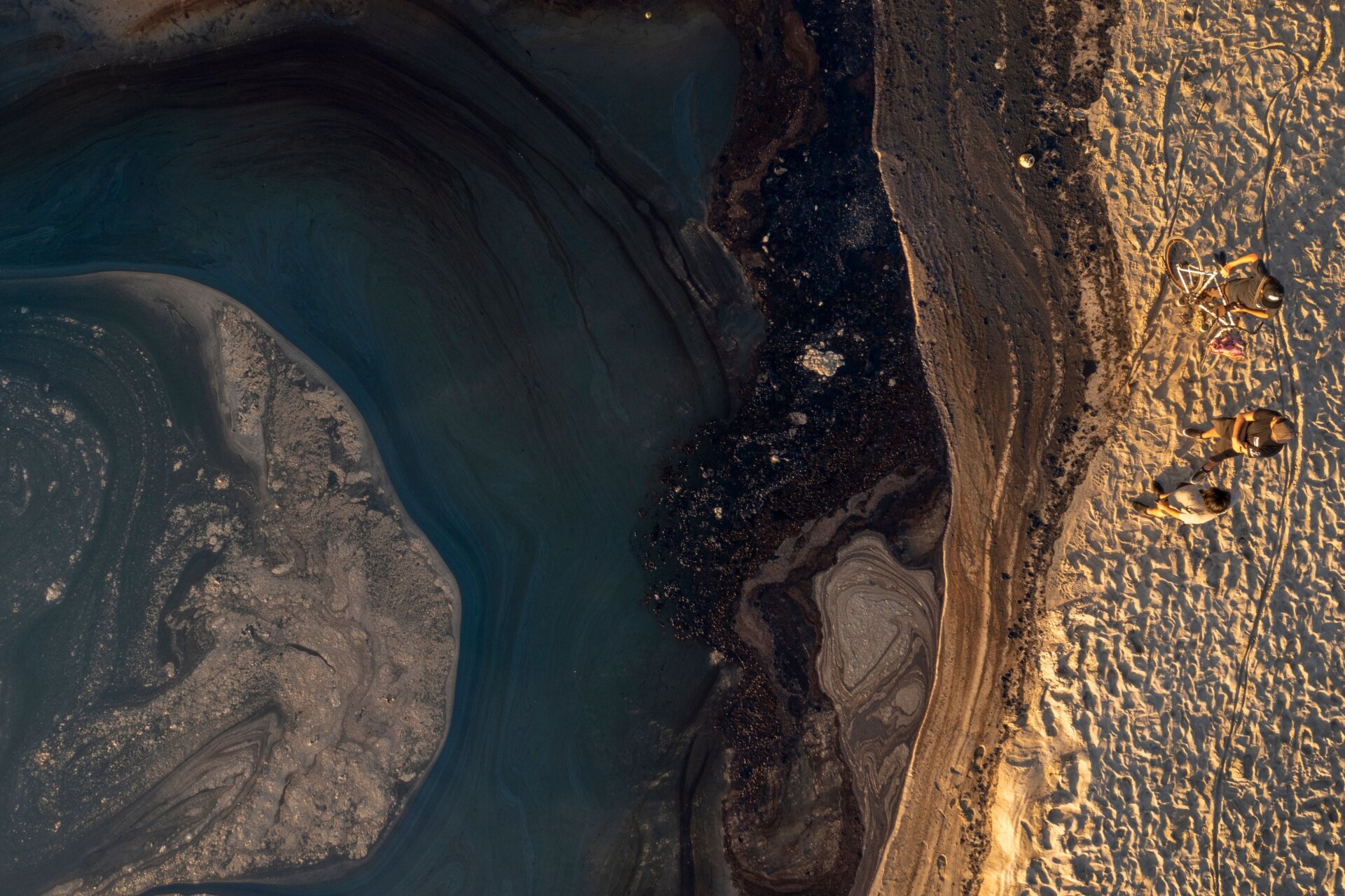 People overlook oil against a berm of sand to keep it from flowing from the ocean into the Santa Ana River as an oil spill from an offshore oil rig reaches the shore and sensitive wildlife habitats in Newport Beach, California.