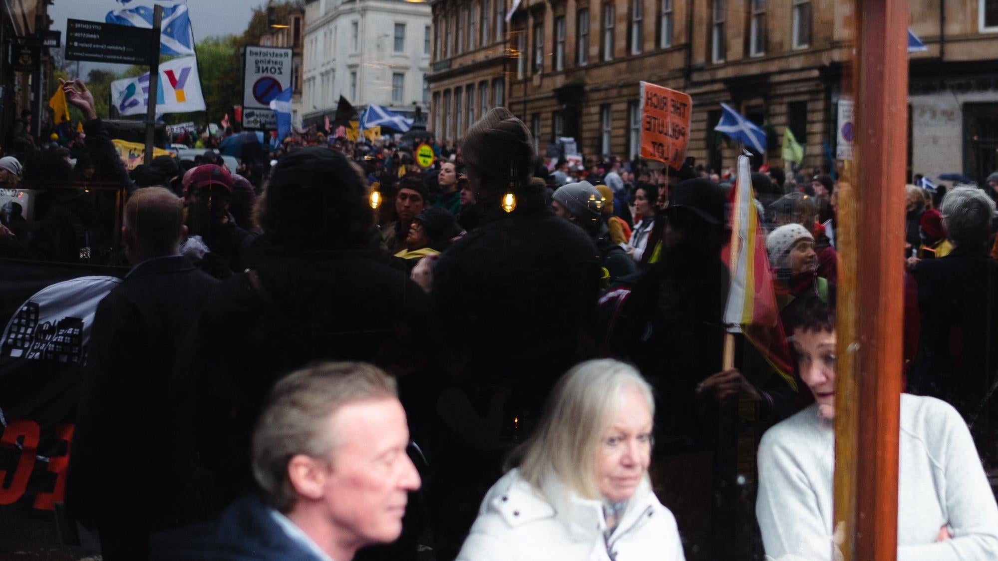 Protesters in the street reflected in the glass of a restaurant as onlookers stare out.