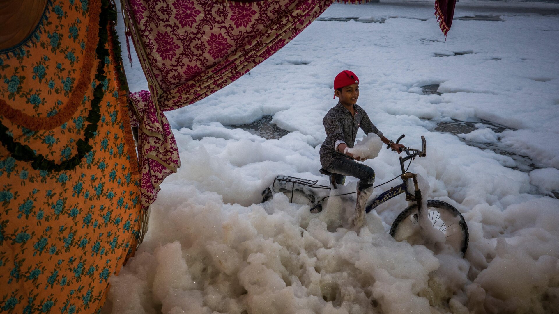  A child sits on a bicycle as he poses for a photograph taken by another child (unseen) at the banks of River Yamuna.
