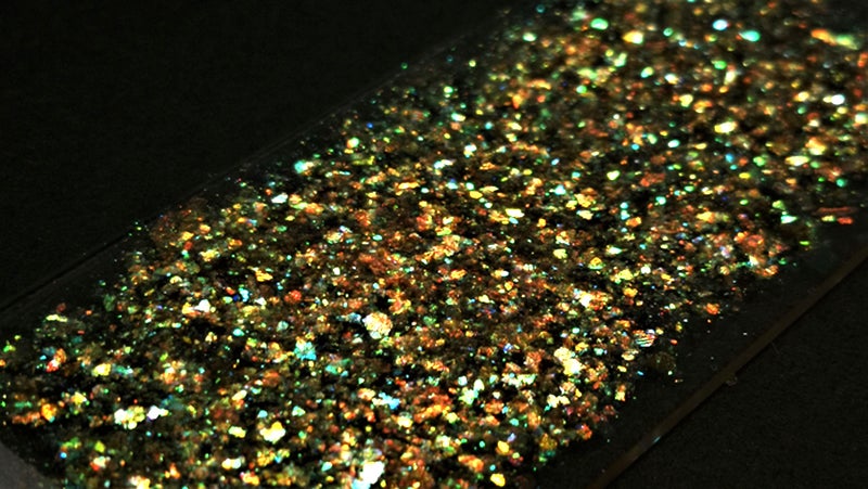 The photograph is a close-up of the glass slide that has been covered with gold flakes with high lighting contrast and observed at larger angle.