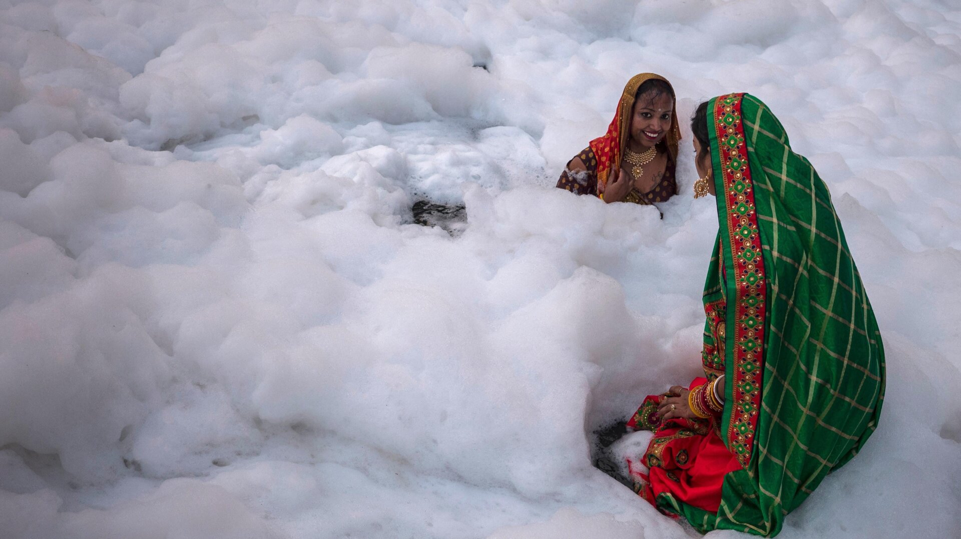 Women take a dip in the waters of River Yamuna amid toxic foam caused by pollution.