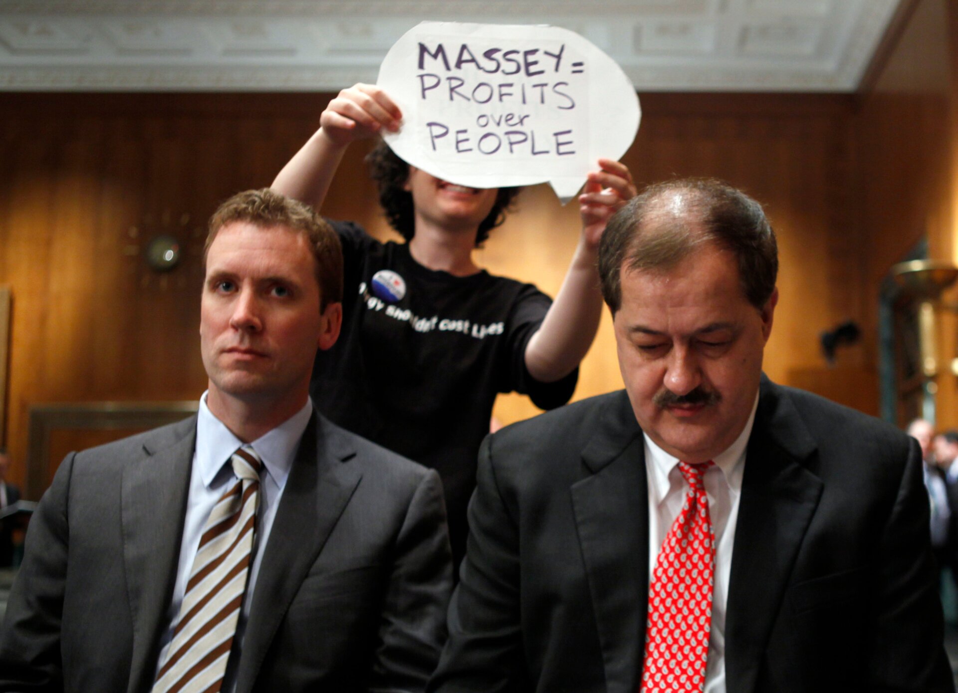 A protester holds a sign behind Vice President of Massey Energy Company and general council Shane Harvey, left, and Massey Energy Company Chief Executive Officer Don Blankenship as they wait to testify on Capitol Hill in Washington, Thursday, May 20, 2010.