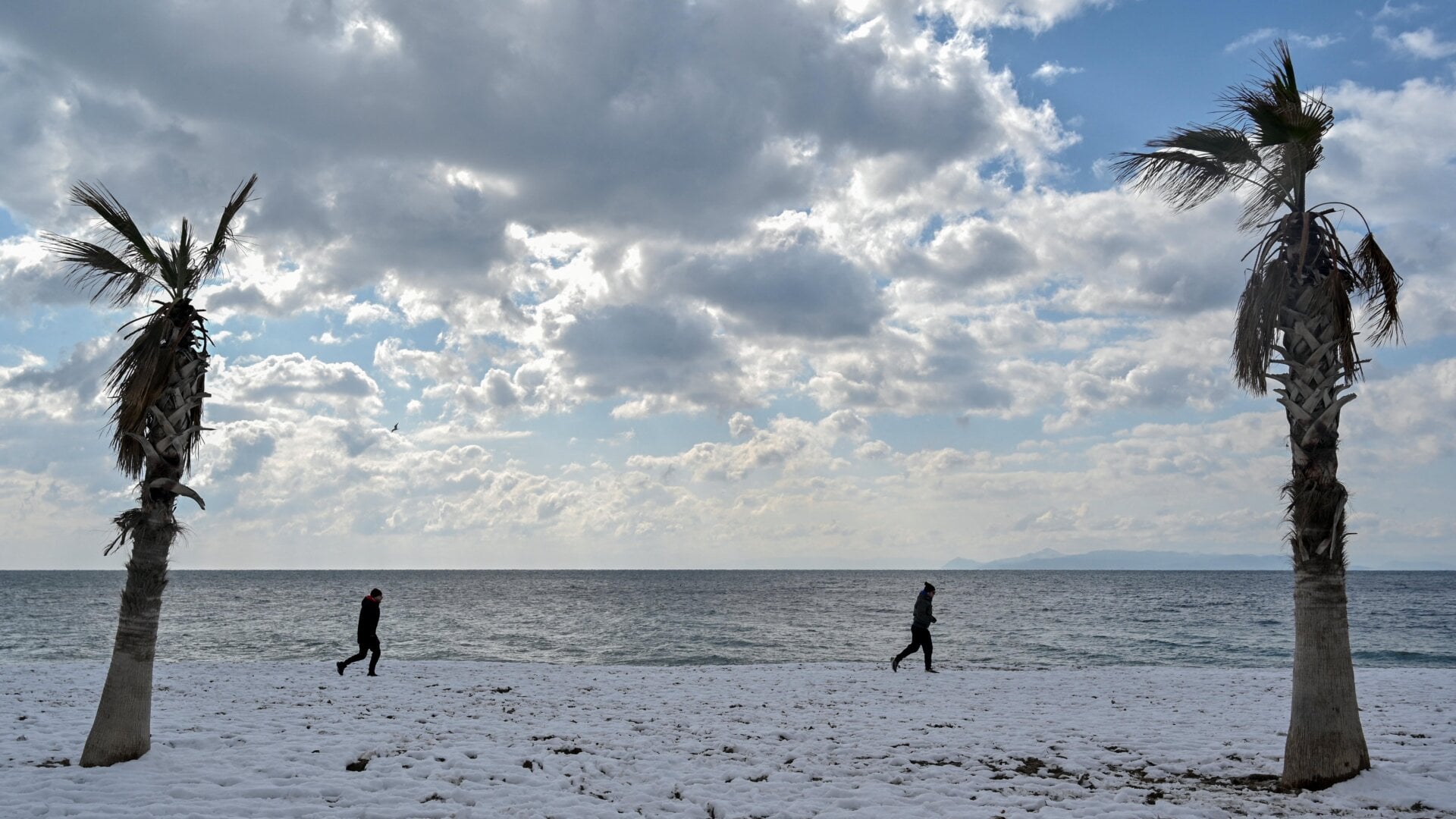 People walk along a snow-covered beach in Athens on January 25, 2022.