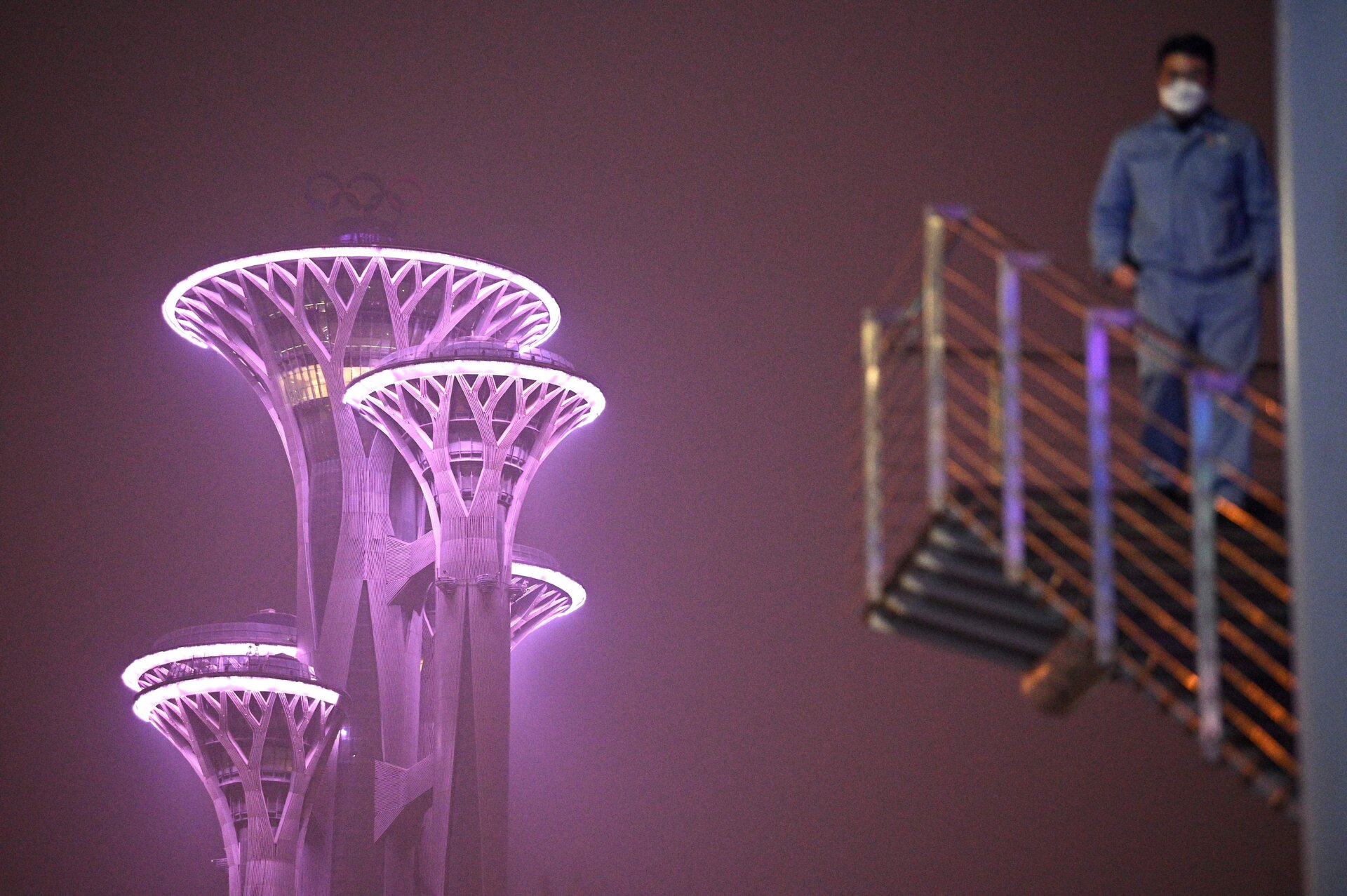 A man walks down some stairs as the Beijing Olympic Tower is seen during a smoggy day in Beijing on January 24, 2022. 