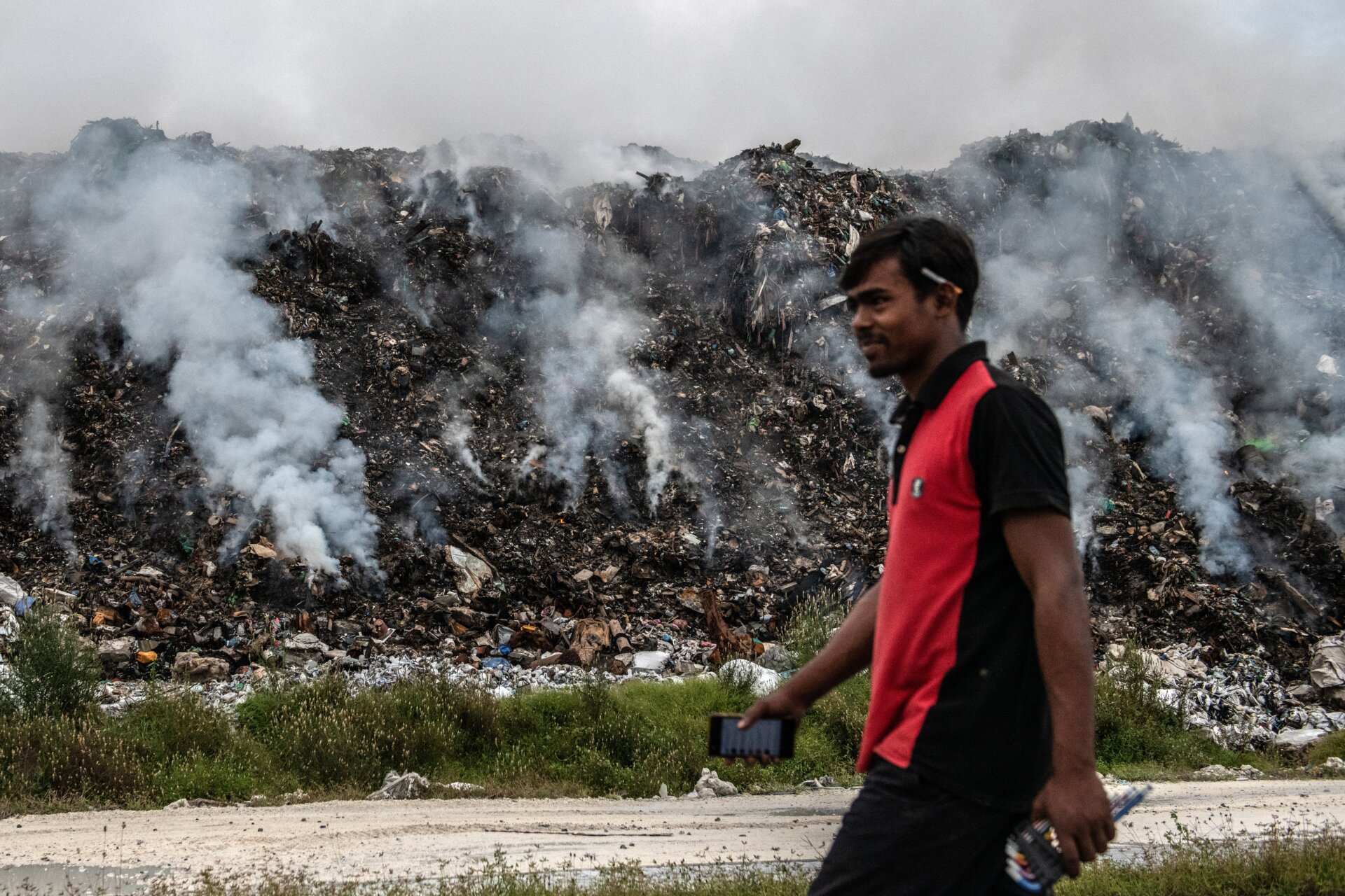 A man walks past smoldering trash on Thilafushi in December of 2019.
