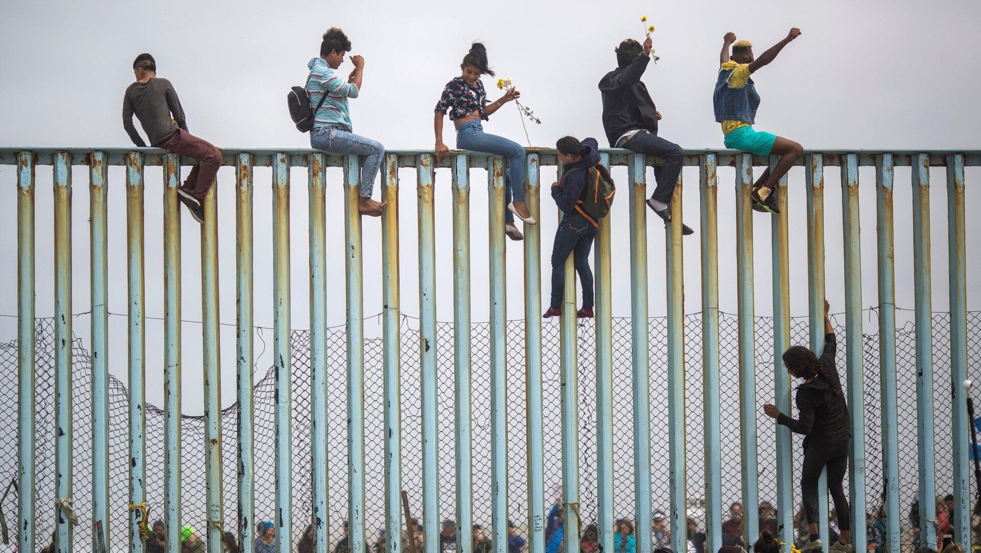 People climb a section of border fence to look toward supporters in the U.S. as members of a caravan of Central American asylum seekers arrive to a rally on April 29, 2018 in Tijuana, Baja California Norte, Mexico