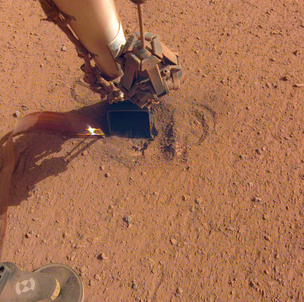 InSight’s arm tamping down the soil over the Mole, which is buried underground. The Mole ended up stuck in the soil, unable to dig deep enough, and the instrument was abandoned.