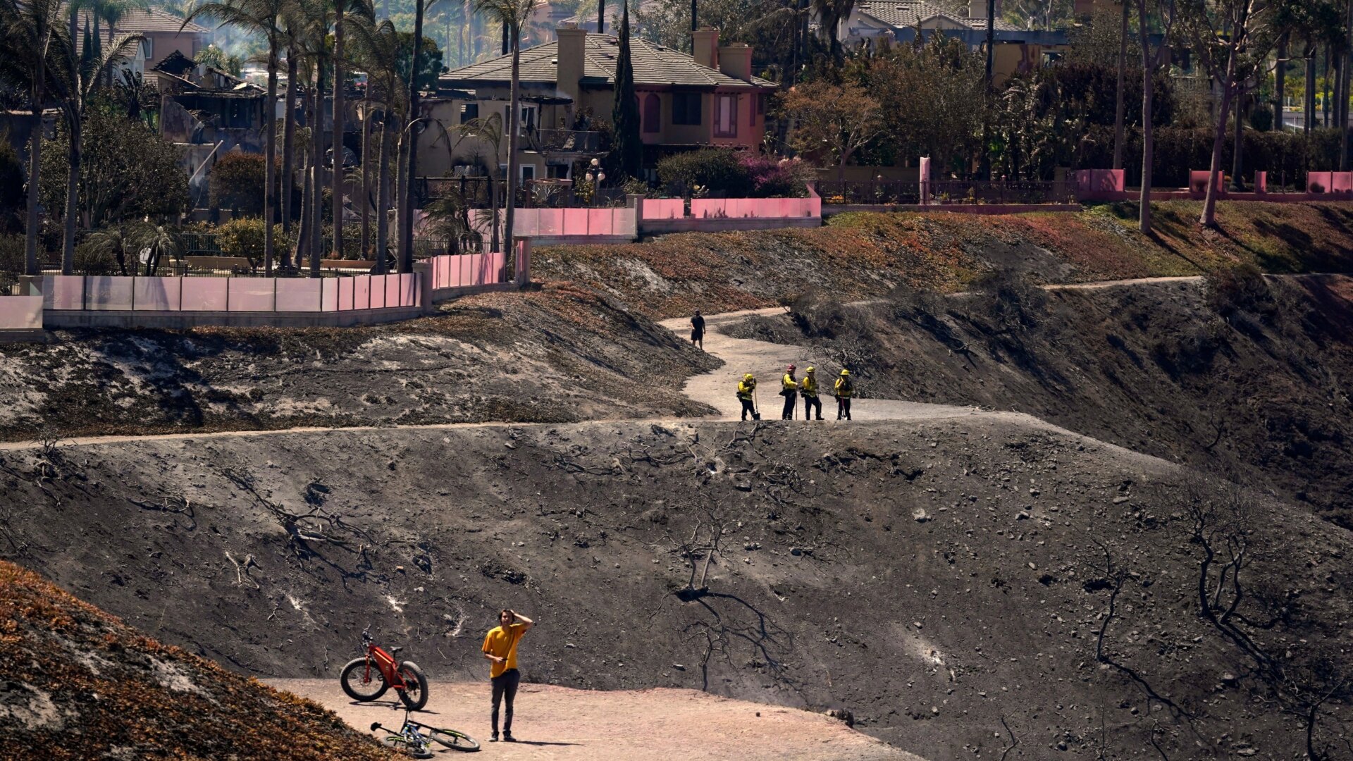 Firefighters and residents stand on a fire road where the Coastal Fire jumped and burned several homes Thursday, May 12, 2022, in Laguna Niguel, Calif.